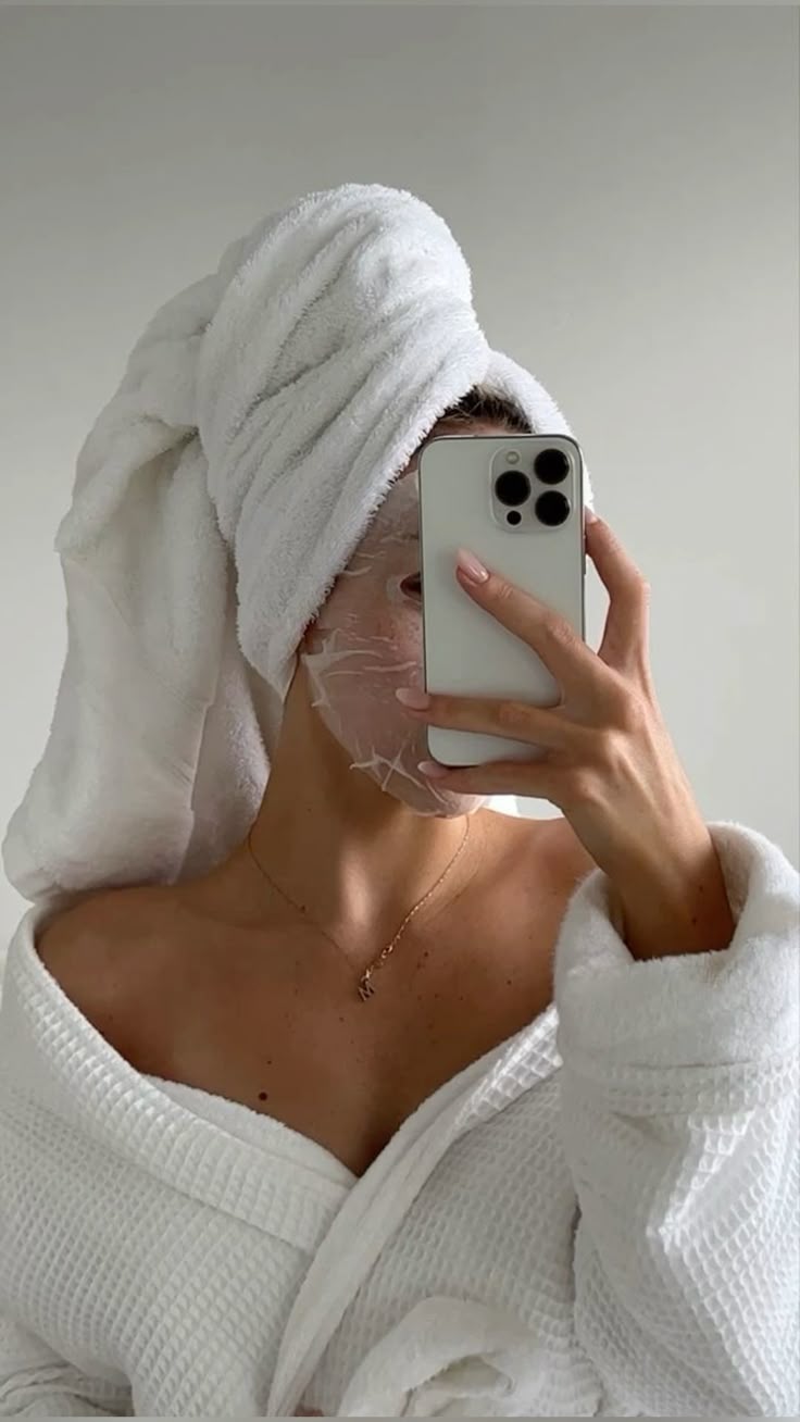 A woman lying down with a towel wrapped around her head, her face glowing with facial oil. She has a peaceful expression, enjoying a skincare treatment.