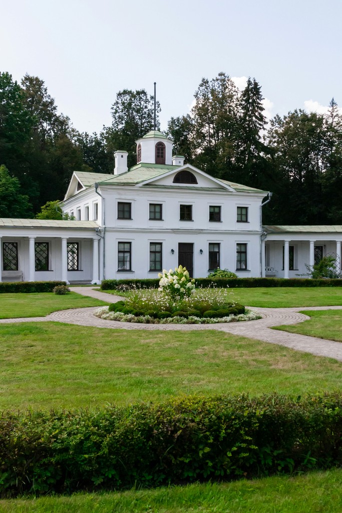 White manor house with colonnades and manicured gardens