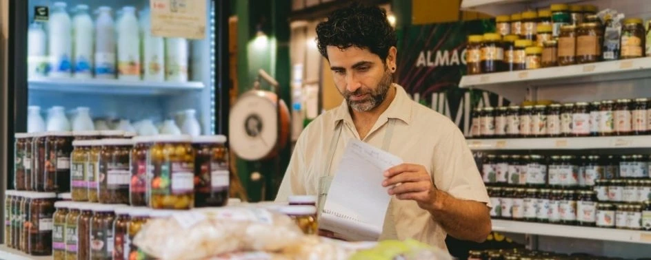 Homem branco, de barba grisalha, segurando um caderno em loja de alimentos orgânicos.