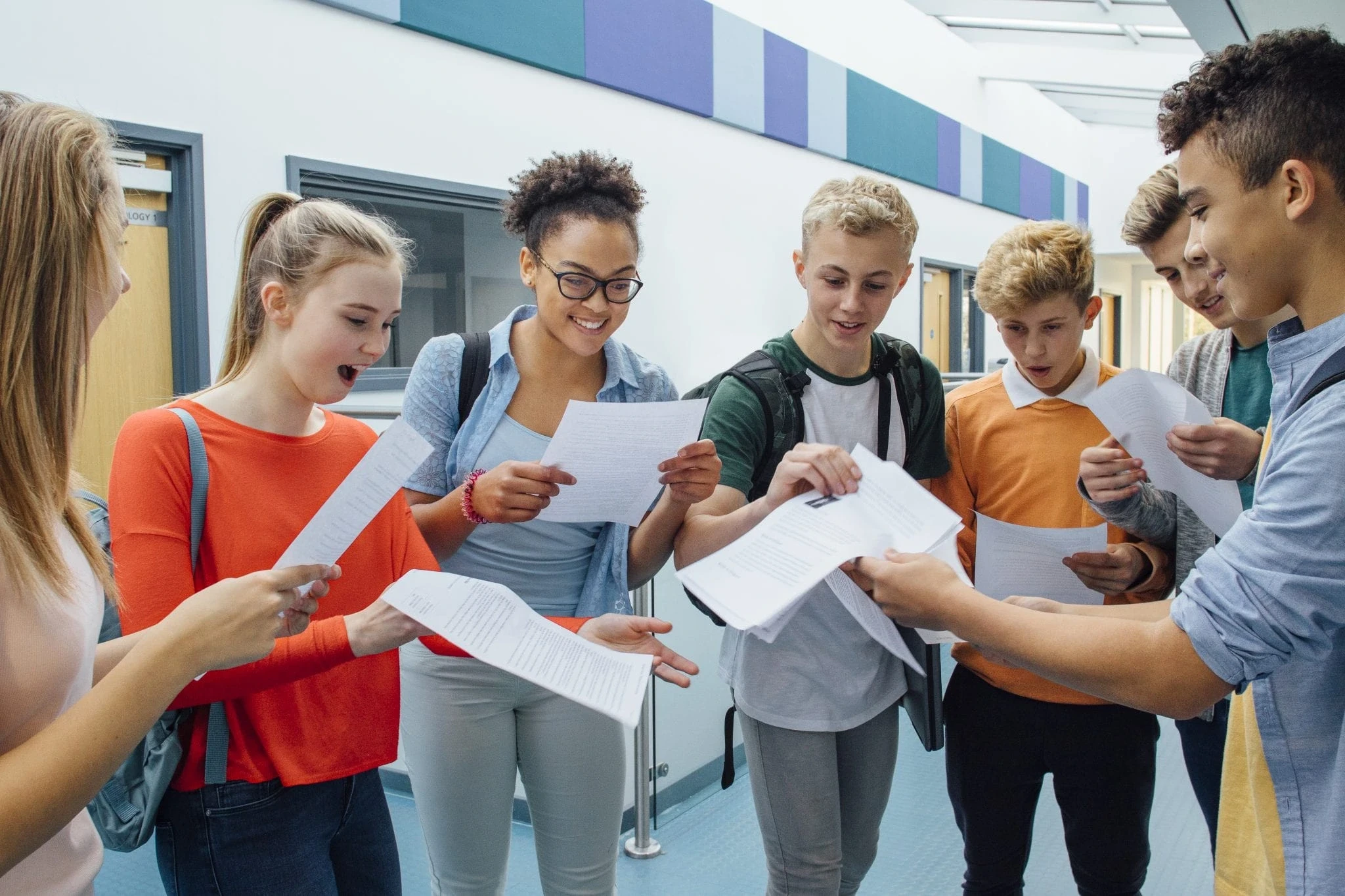 High school students in RISE Research or summer programs celebrate academic results, smiling and reacting with excitement in a diverse school hallway setting.