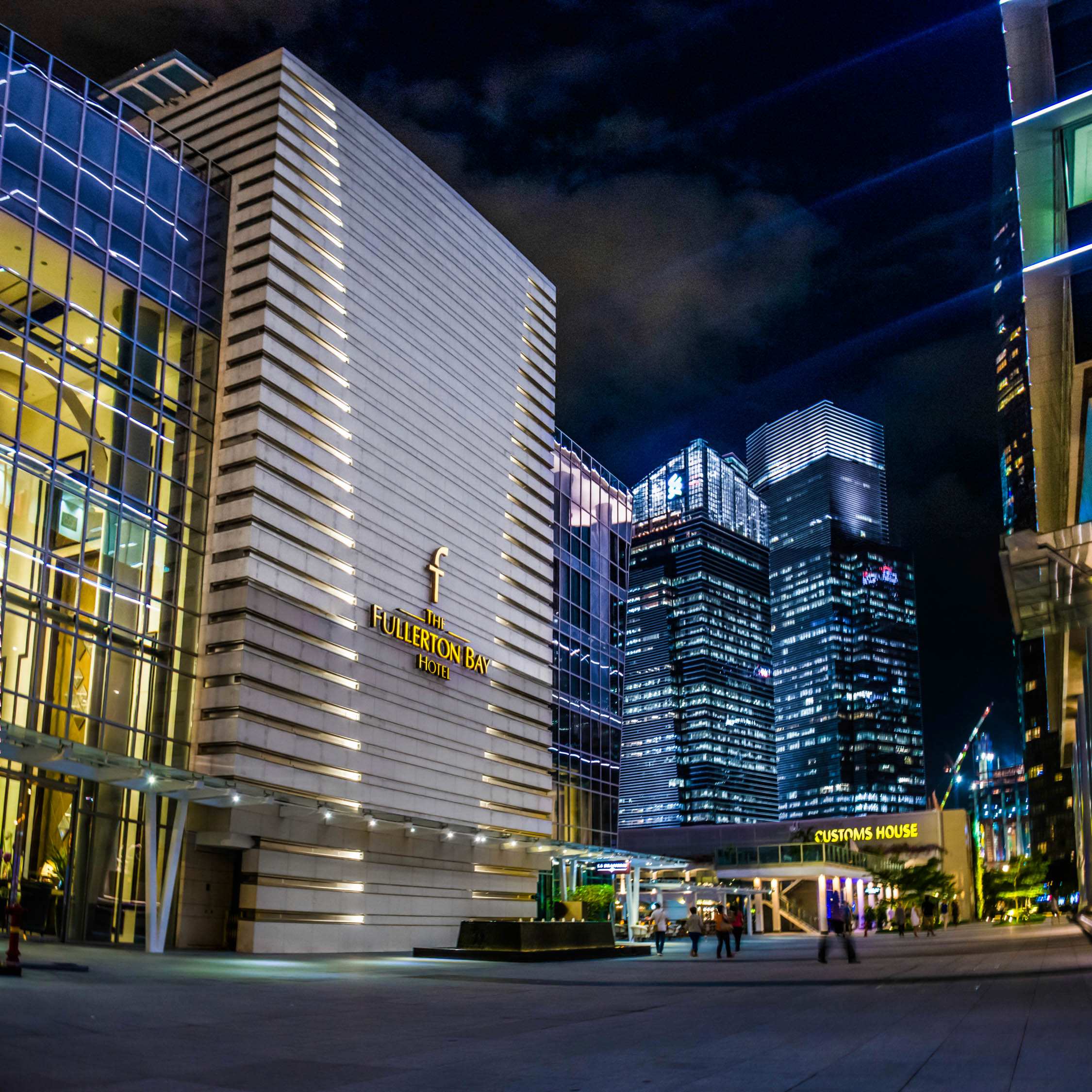 Modern glass and stone buildings with illuminated facades and "Four Seasons" signage at night in a city center.