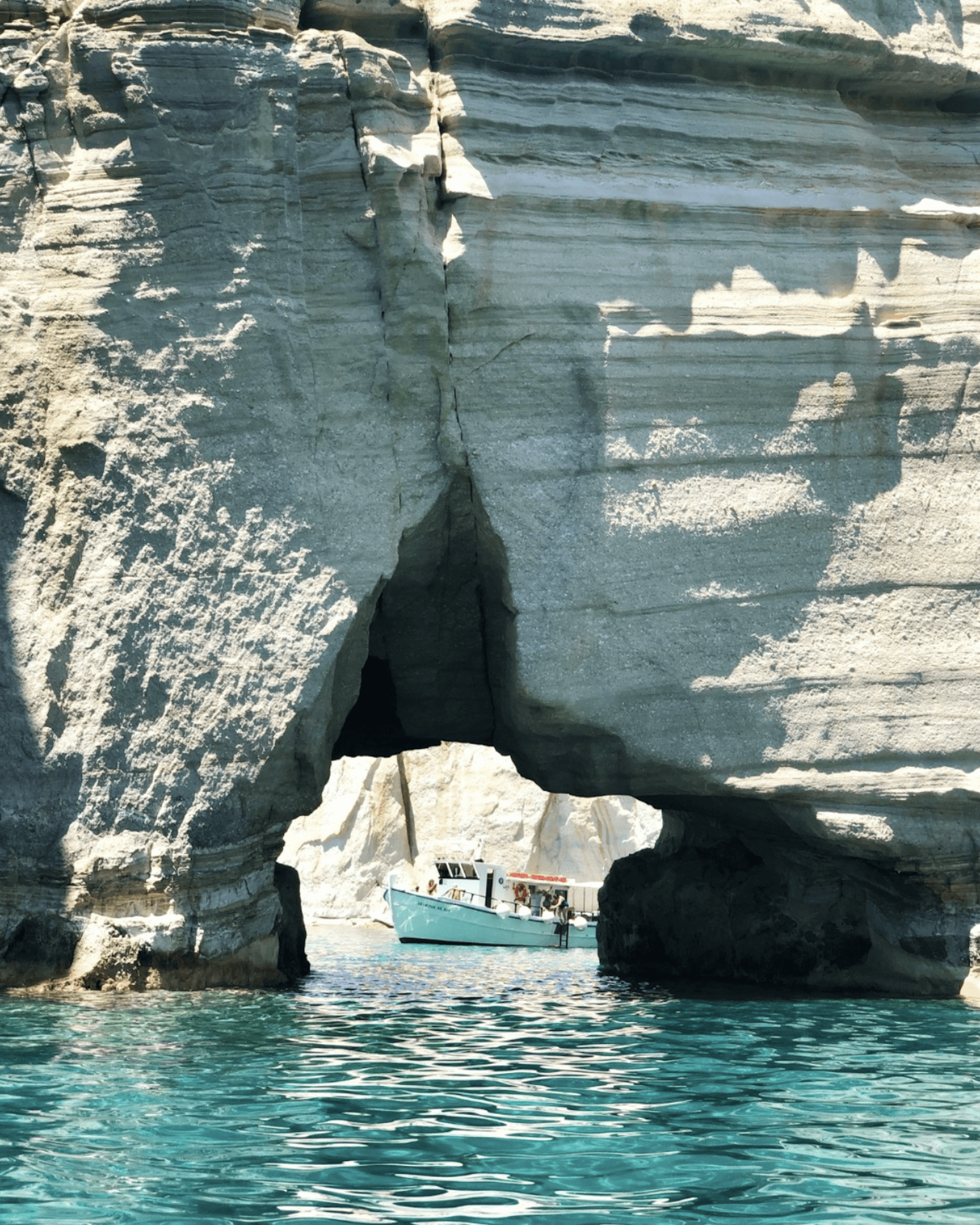 Polyaigos cliff view and a tourist boat going through the cave.