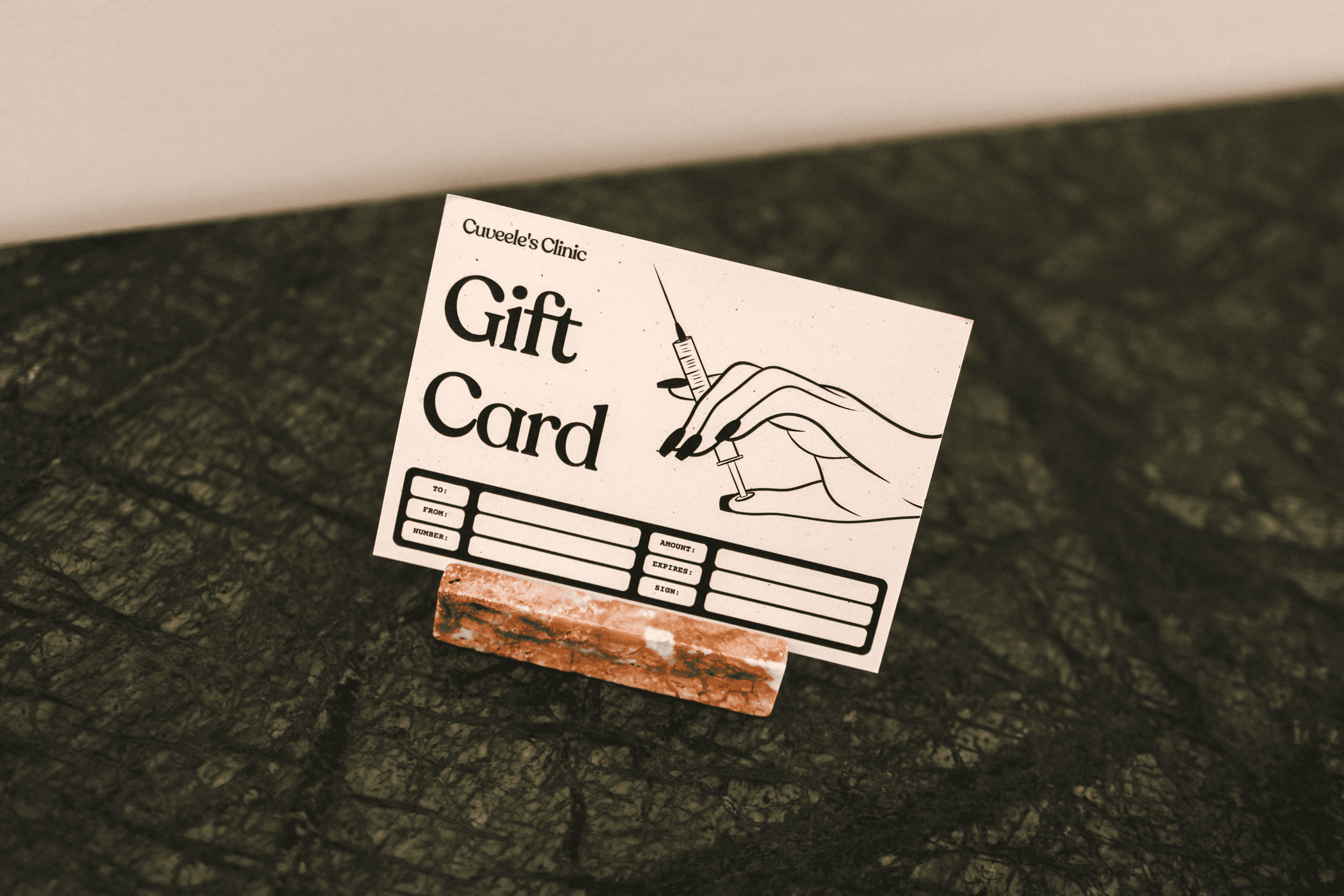 Een cadeaubon van Cuveele's Clinic gepresenteerd op een groen marmeren oppervlak.