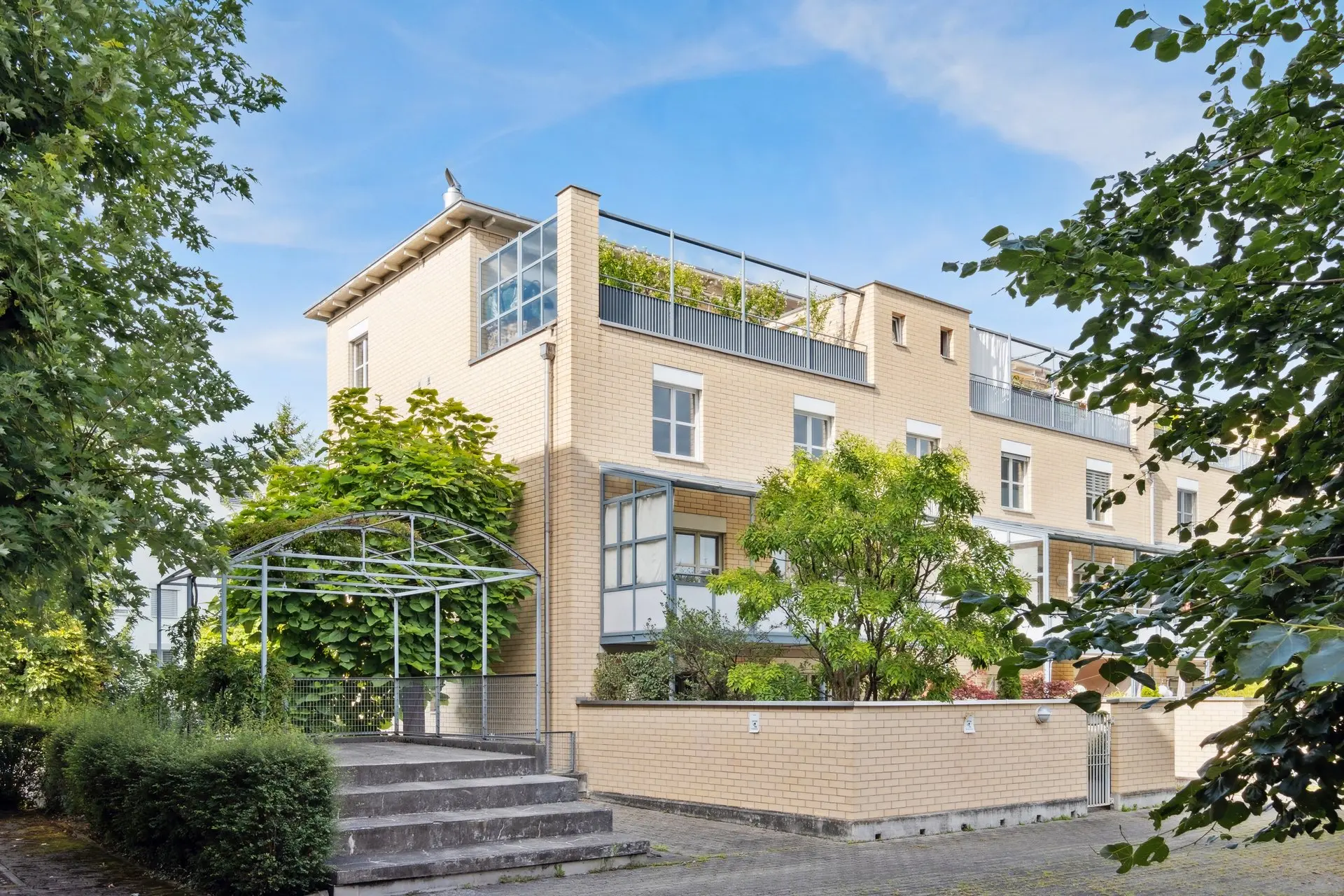 Mehrfamilienhaus mit Treppeneingang, umgeben von Begrünung