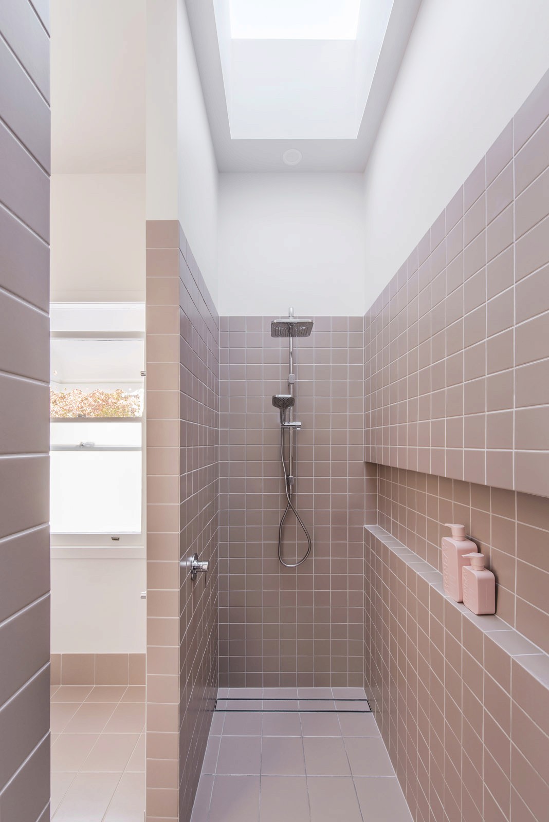 Walk-in shower with pink tiled walls, skylight, and recessed shelf for toiletries