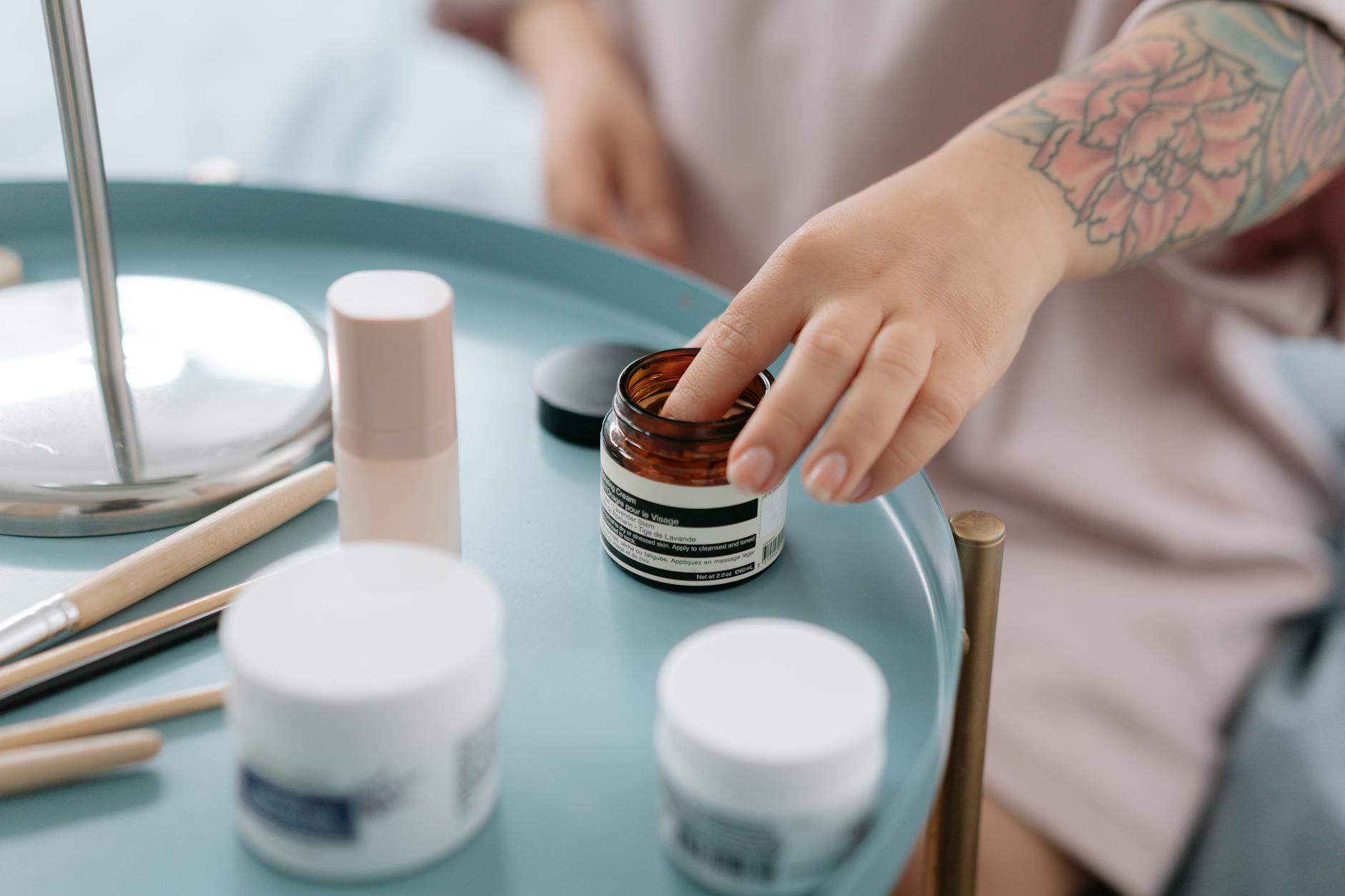 A close-up shot of a hand reaching for skincare creams on a blue tray indoors.
