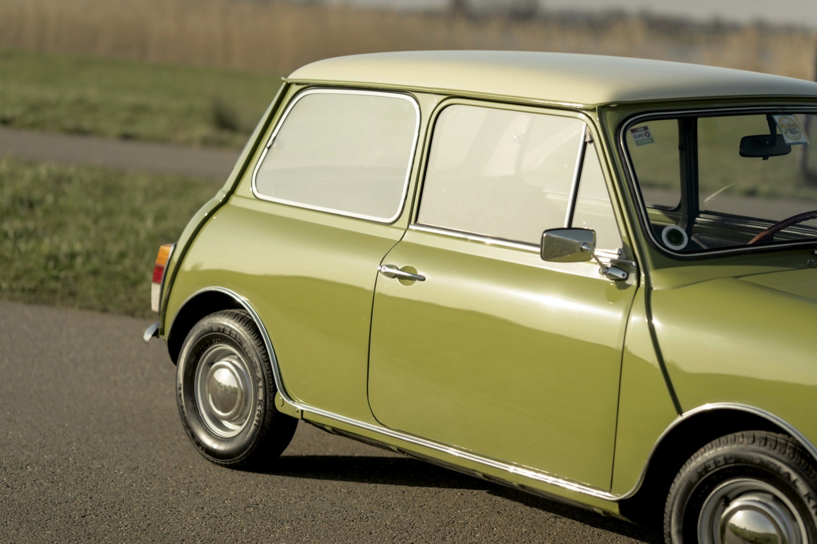 A close-up of a vintage lime green car parked on a road near grassy fields.