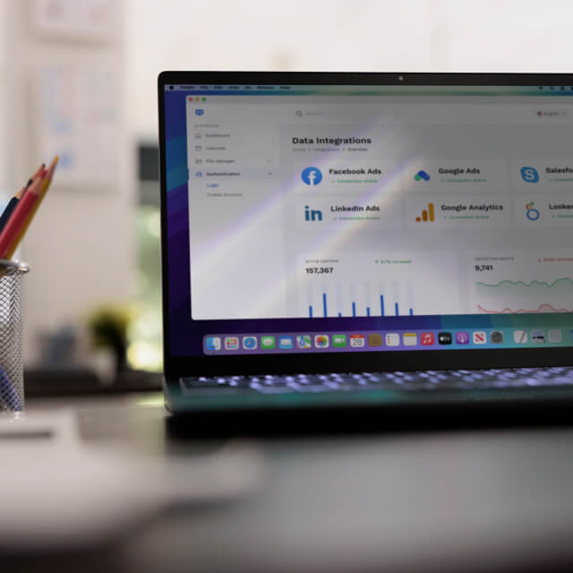 A laptop on a desk displays a data integrations dashboard with analytics for Facebook Ads, Google Ads, LinkedIn Ads, and Google Analytics.