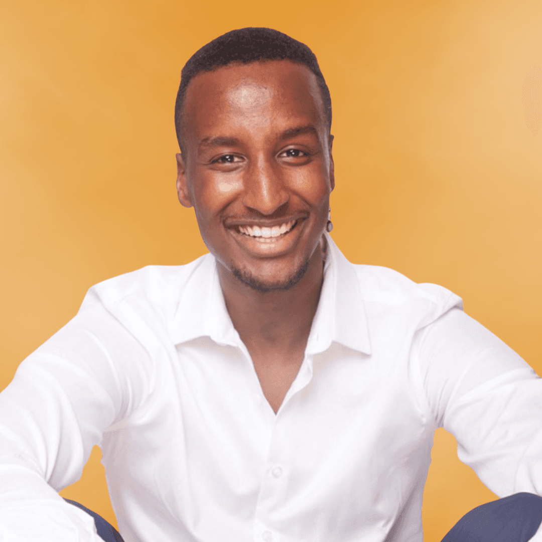 A smiling person with short hair wearing a white shirt, sitting against a bright yellow background.