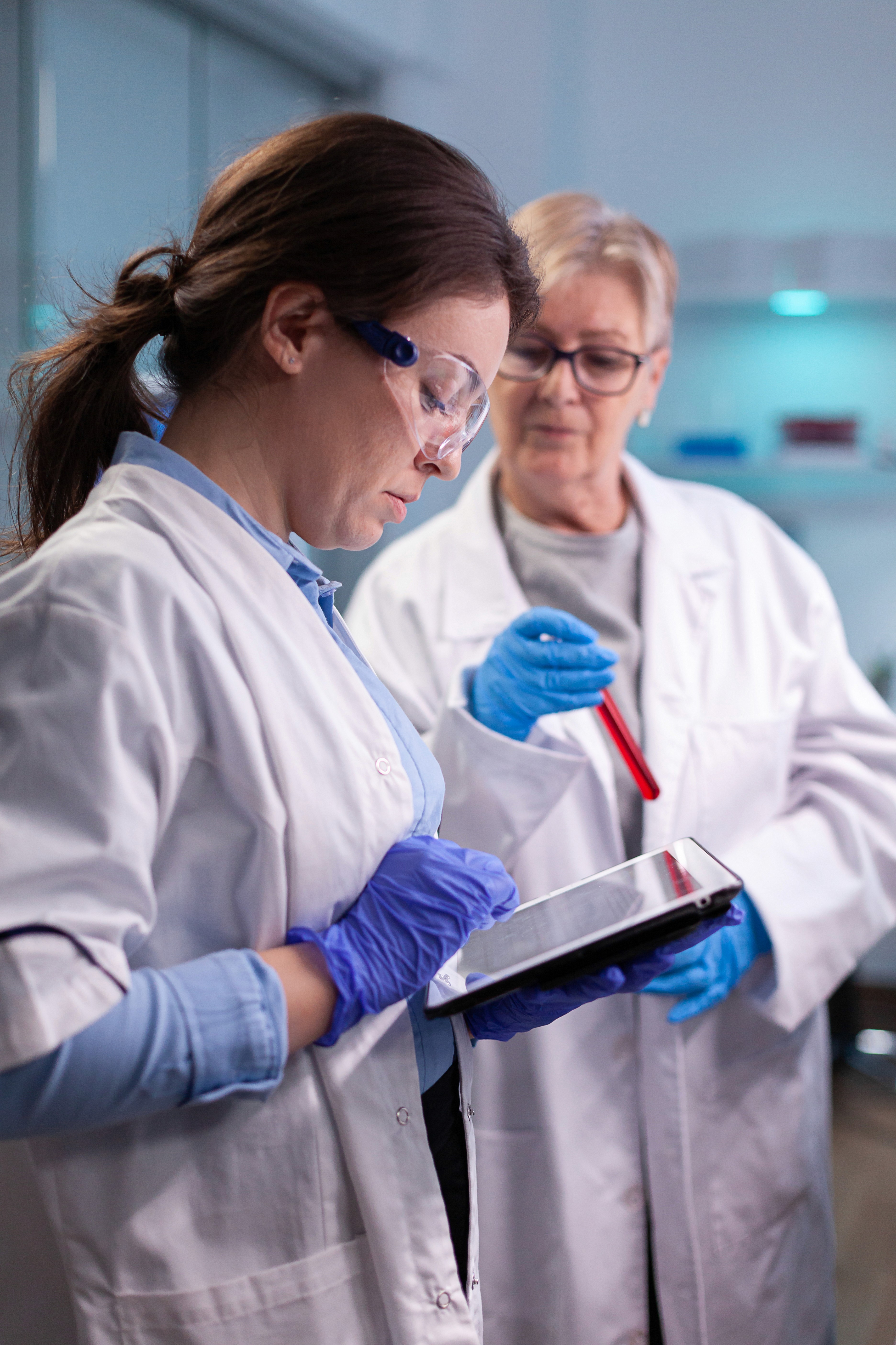 Two scientists in lab coats and safety glasses looking at a tablet and test tube. Research and development concept.