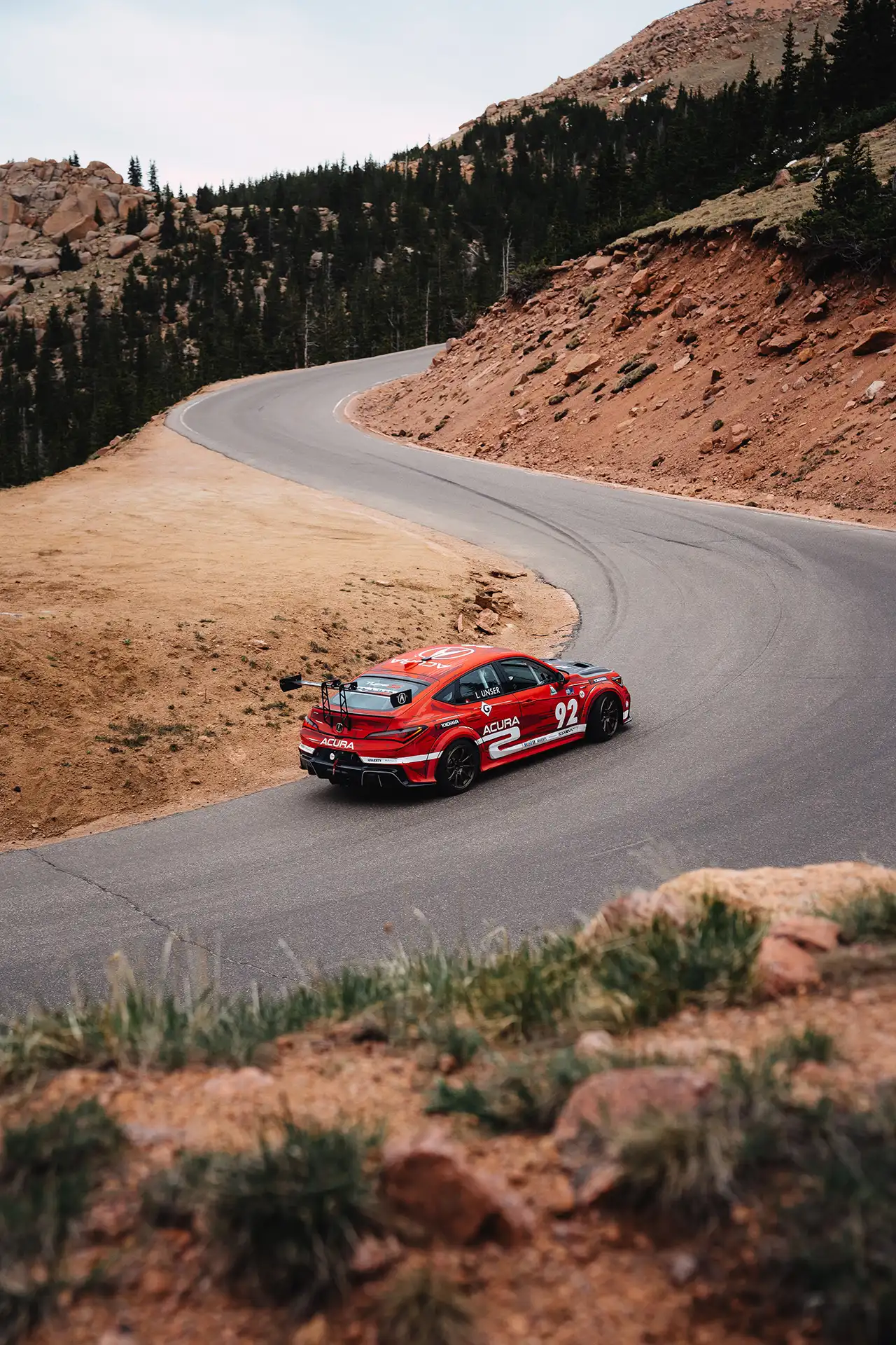 A red Acura race car taking a turn on Pikes peak mountain.