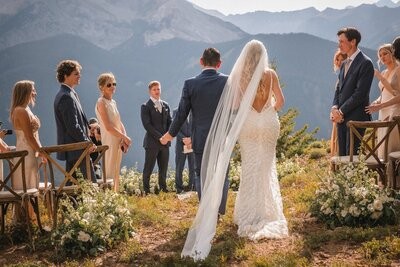 The newlyweds walk up the ceremony aisle, seen from behind with the bride's veil trailing.