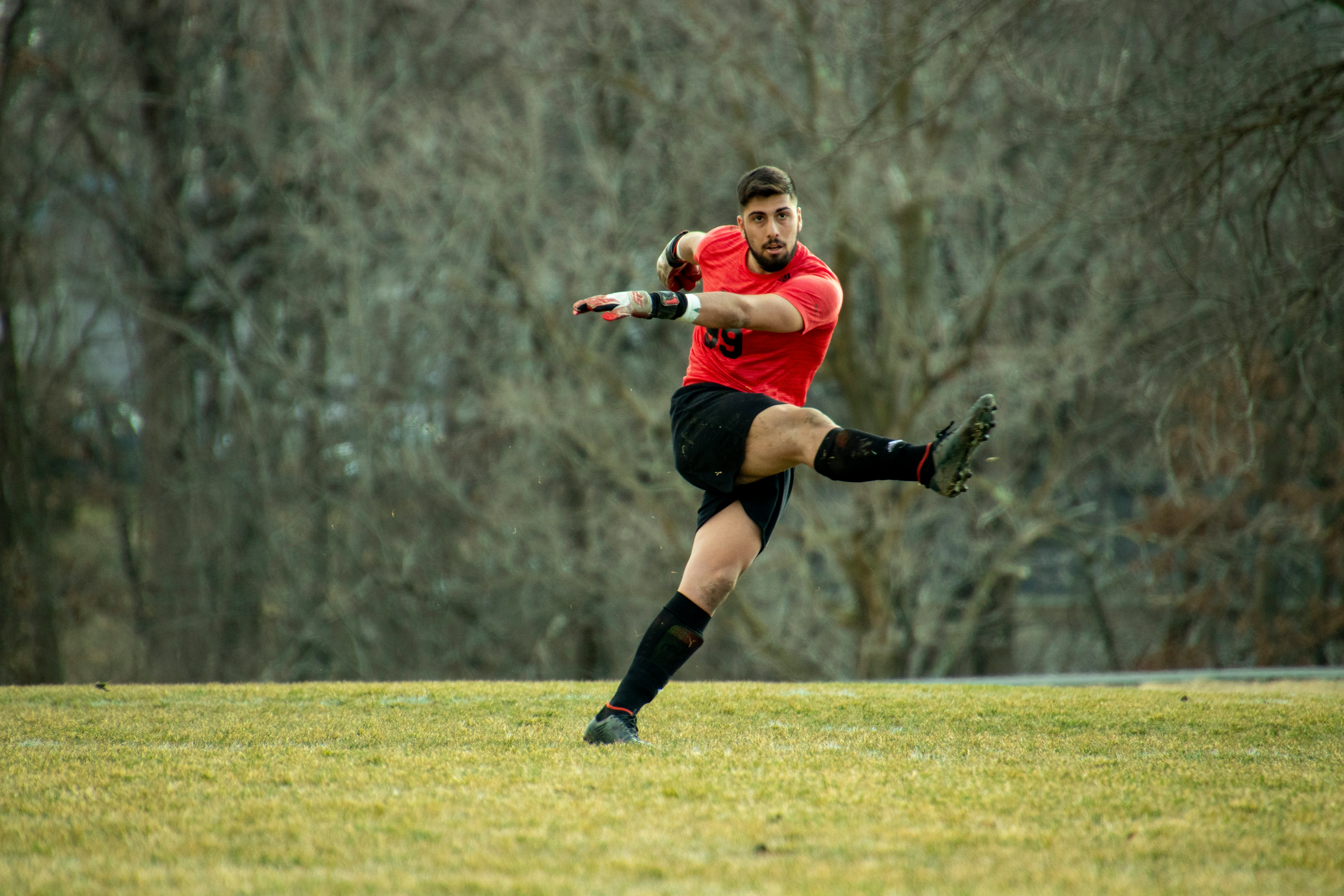 woman in red shirt and black shorts running on green grass field during daytime