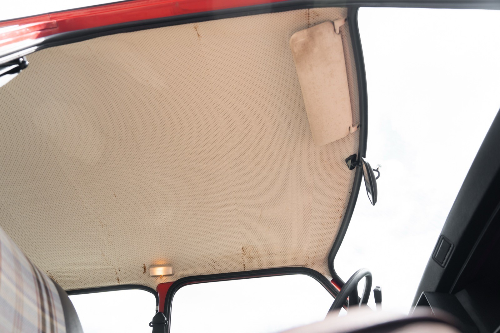 Close-up of a car's interior roof lining, featuring a light-colored material and a handle for opening.
