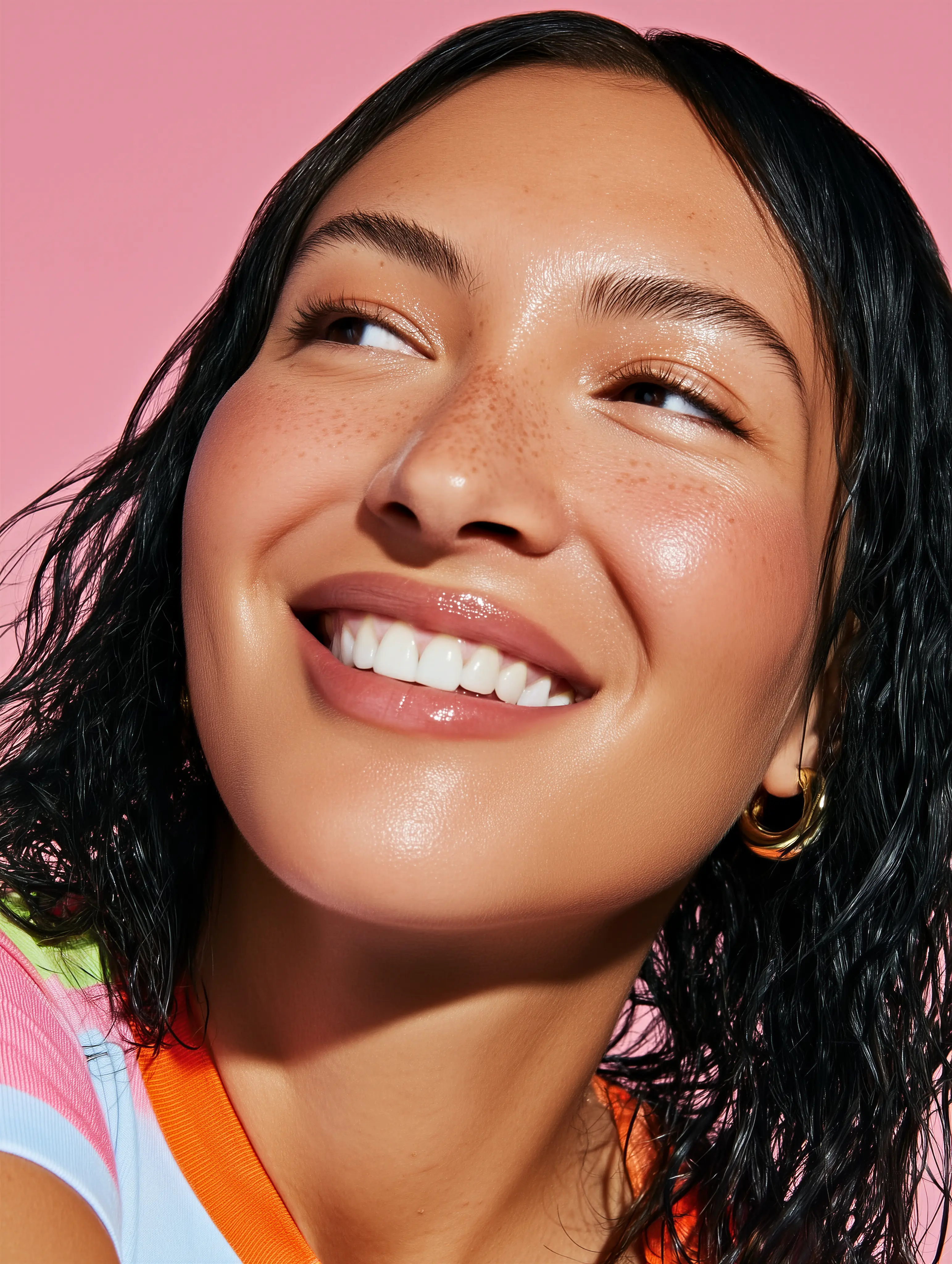 Close-up of a smiling woman with glowing skin against a soft pink background