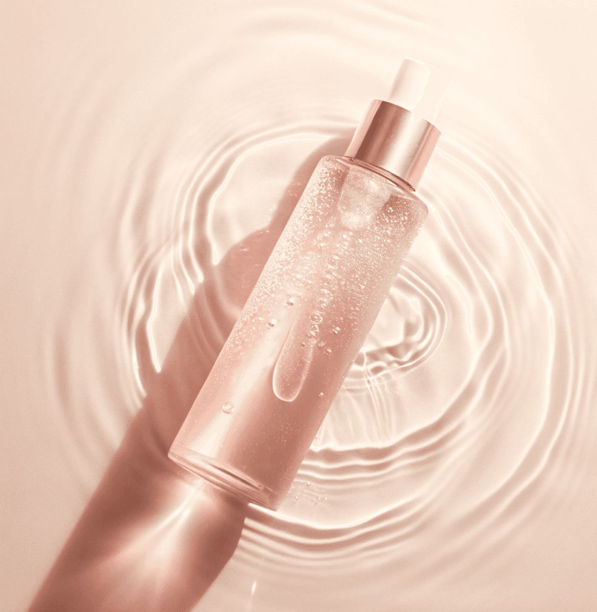 Pink liquid bottle with a blank label floating on rippled water, captured in soft, warm lighting.