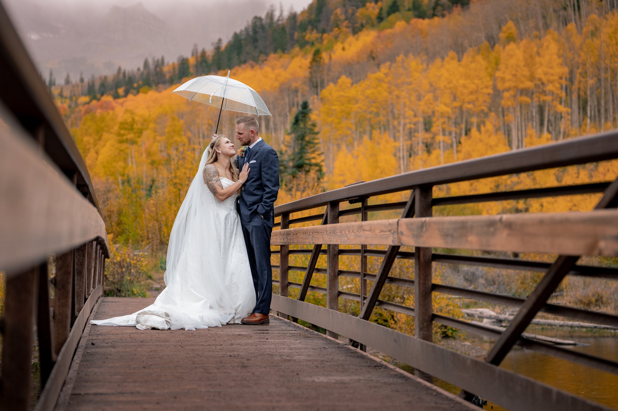 Wedding couple kissing under a clear umbrella on the bridge at Maroon Bells