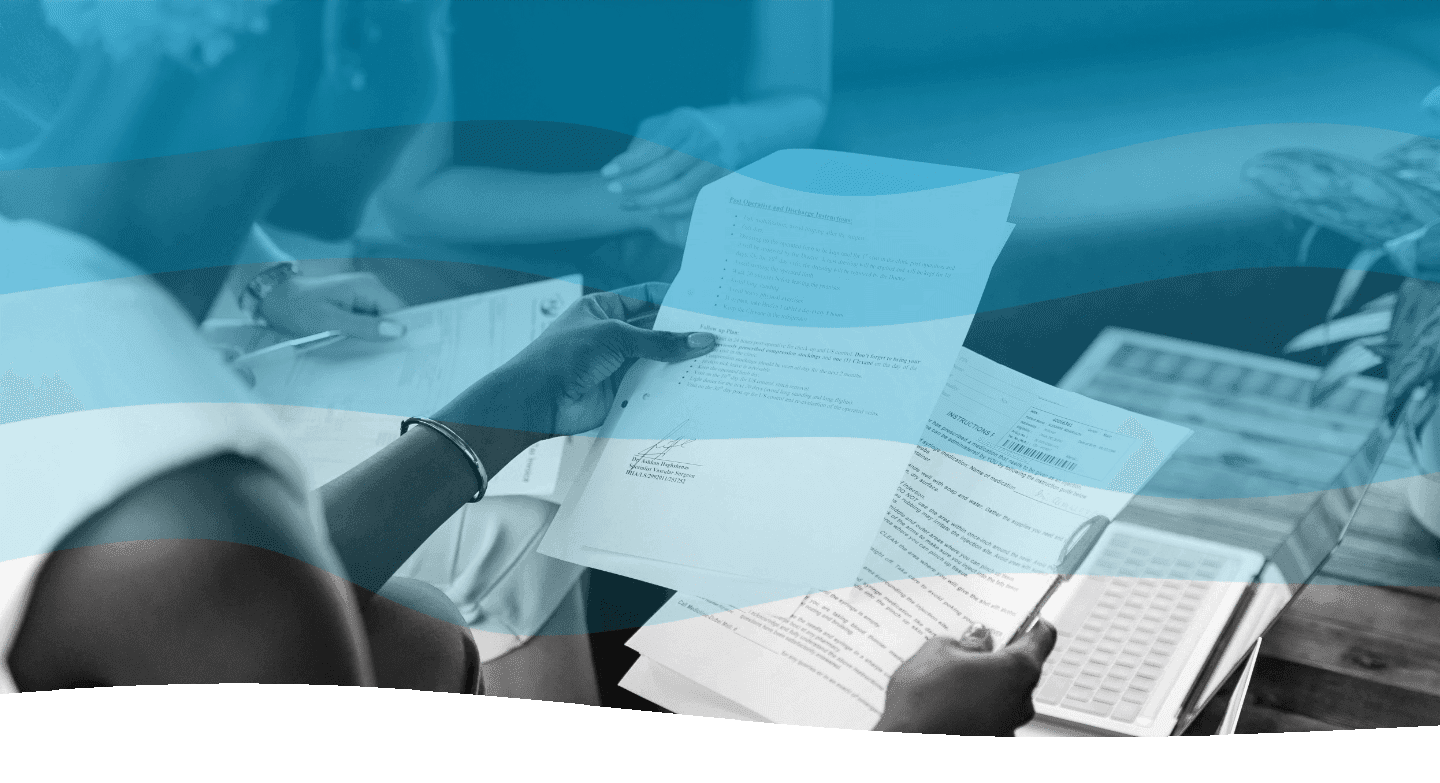 A person reviews documents with charts and graphs, holding a pen, at a table during a meeting.