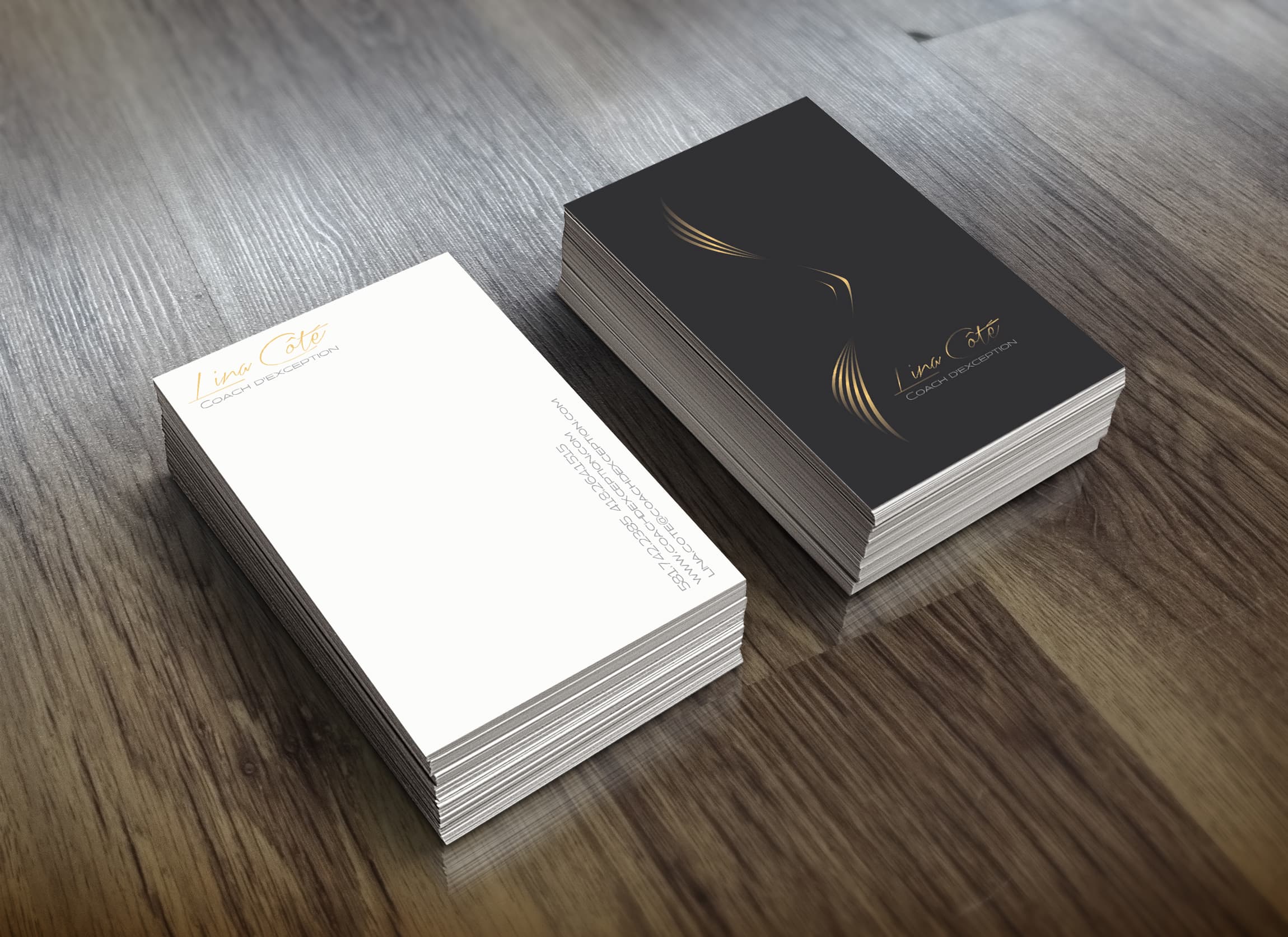 Two stacks of business cards for 'Lina Côté, Coach d’exception' placed on a wood surface. One stack shows the front of the card, which is black with a minimalist gold contour graphic of wings and elegant typography. The other stack shows the back of the card, which is white with gold and grey text containing contact information.