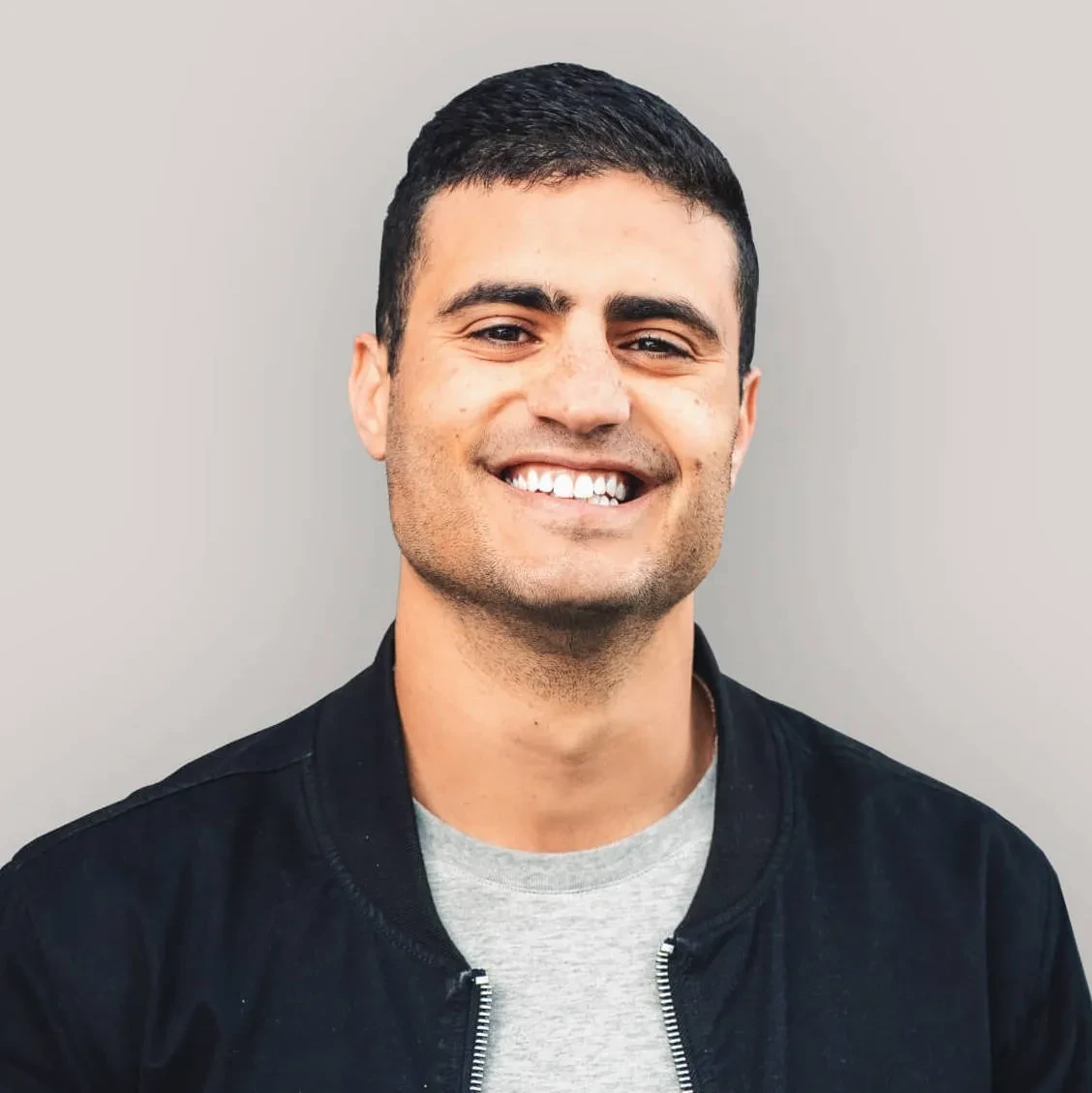 Editorial portrait of a young man with wavy hair in a knit sweater, looking over his shoulder in soft light.
