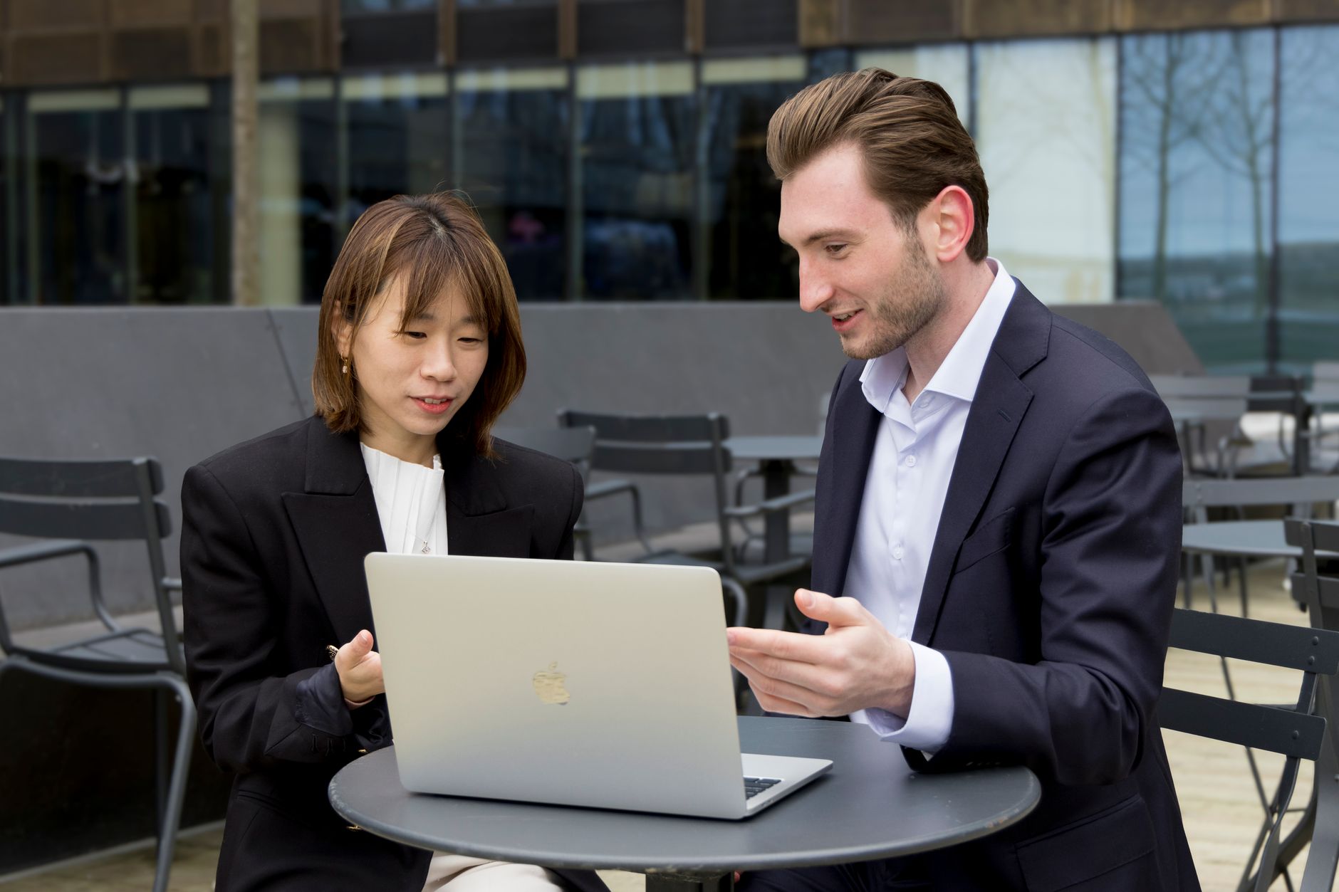 Two professionals collaborating over a laptop during an outdoor business meeting.
