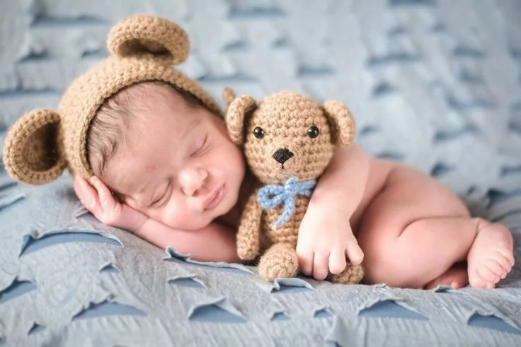 Sleeping newborn in a brown bear bonnet holding a teddy