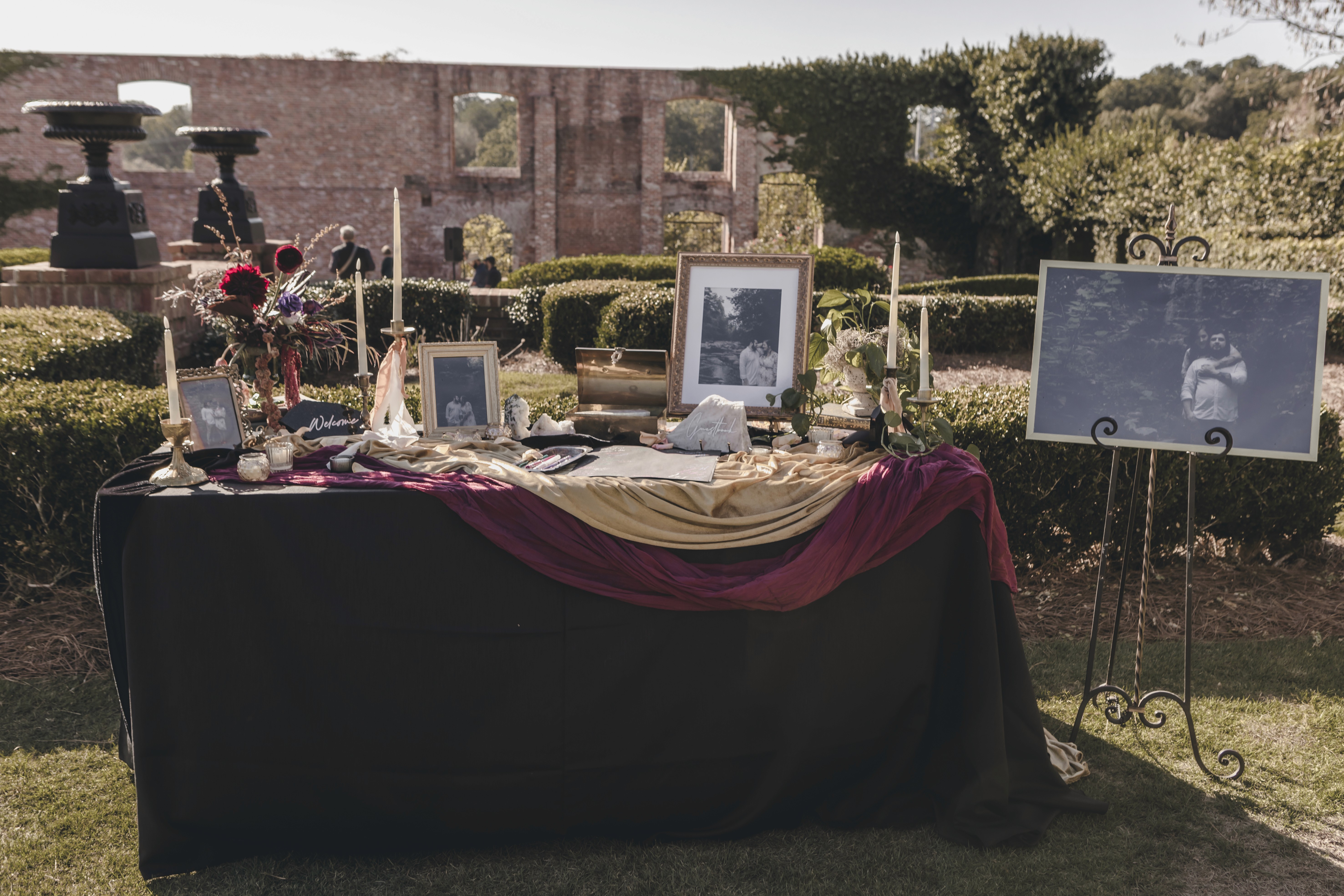Outdoor wedding reception display with framed photographs, candles, and purple floral arrangements.