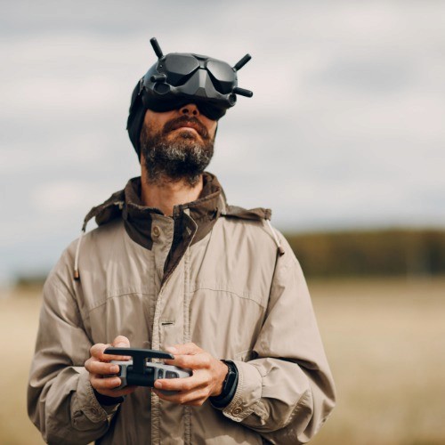 Man standing outdoors wearing FPV goggles and holding a controller