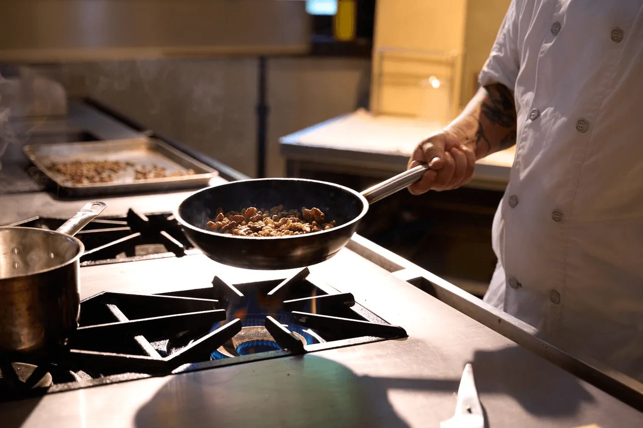 A chef sautéing ingredients in a pan over an open gas flame in the Abrazos kitchen.