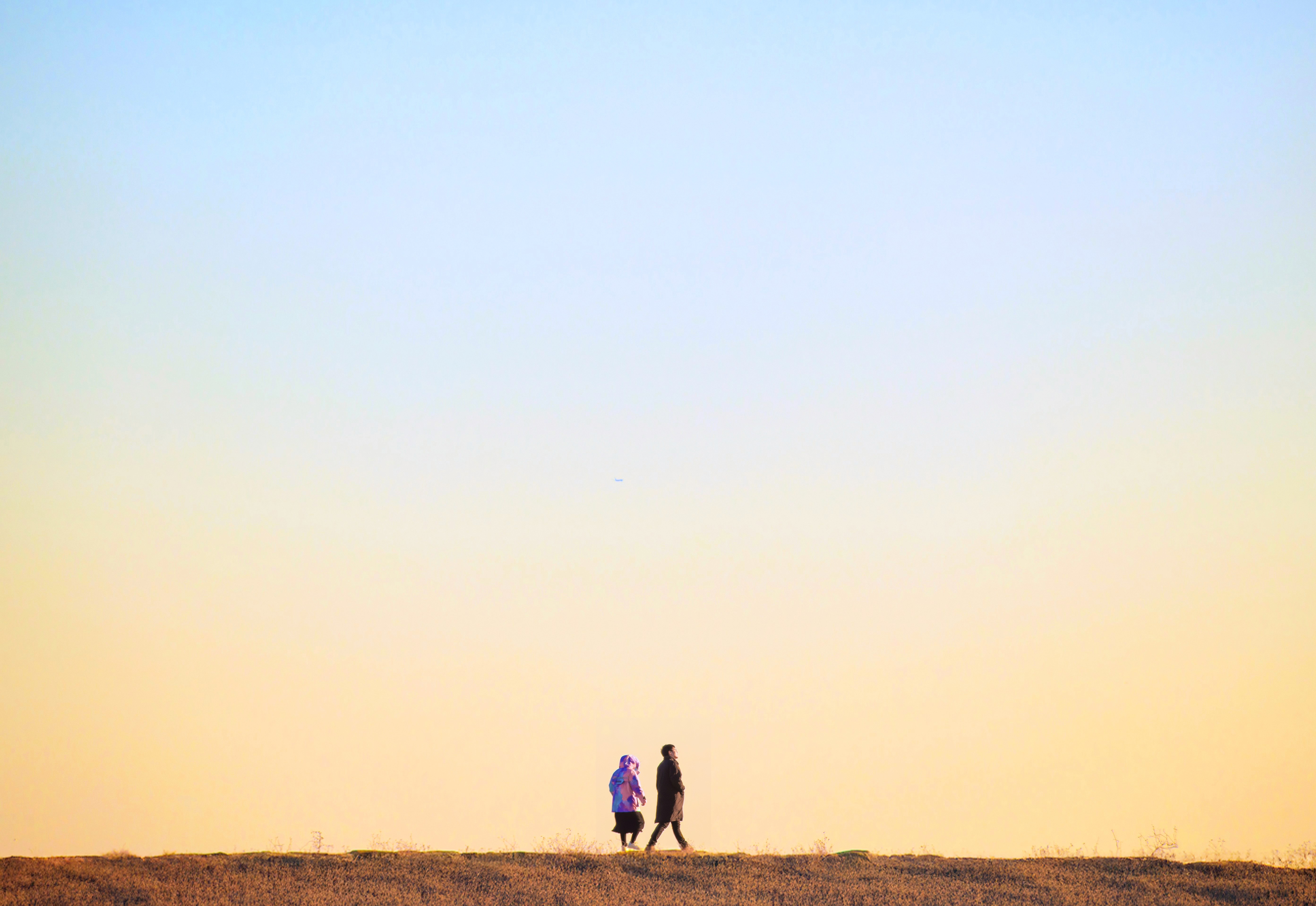 Minimalist outdoor photo of two people walking under a pastel sky, representing simplicity and calm