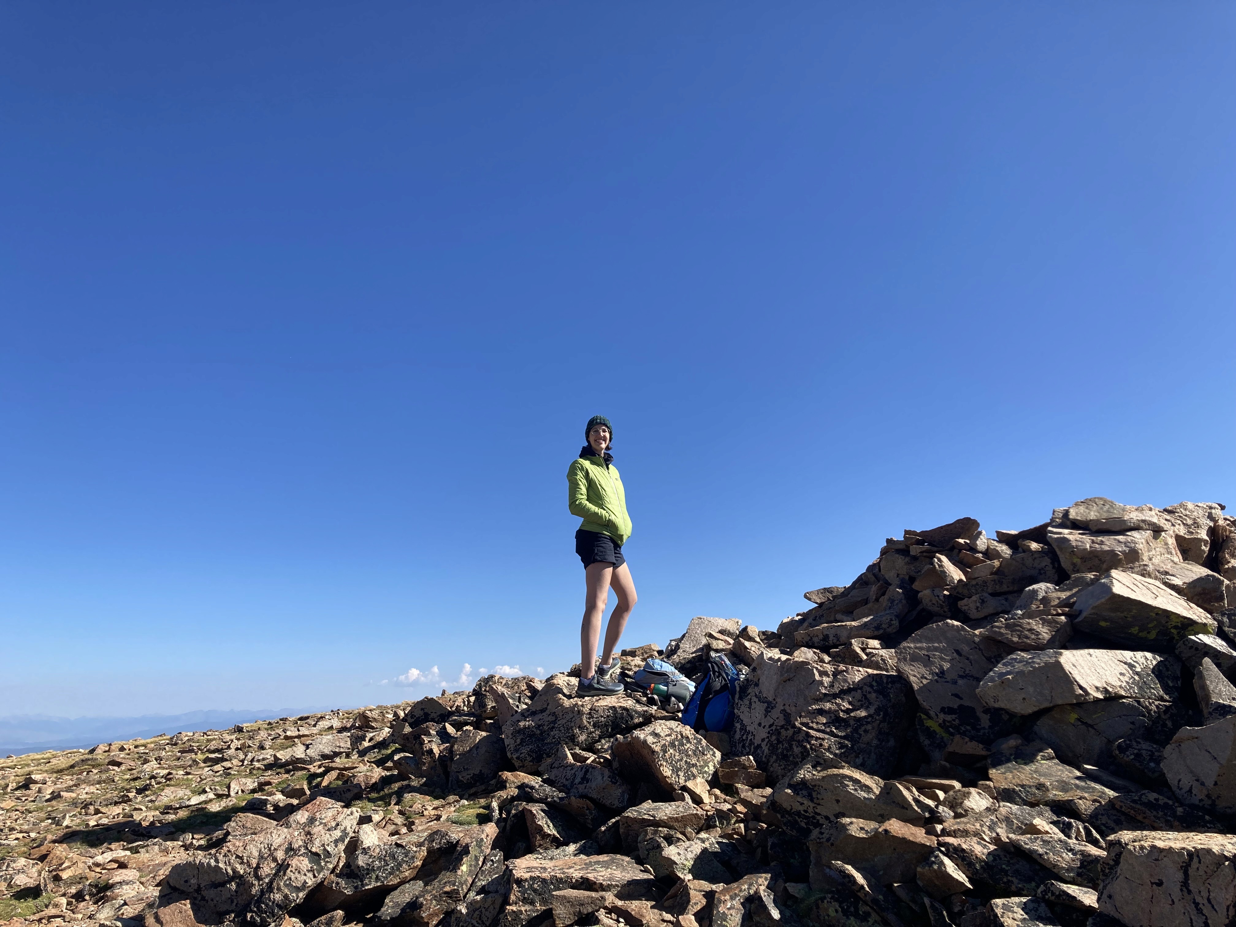 Young woman in green jacket standing on top of a rocky mountain peak