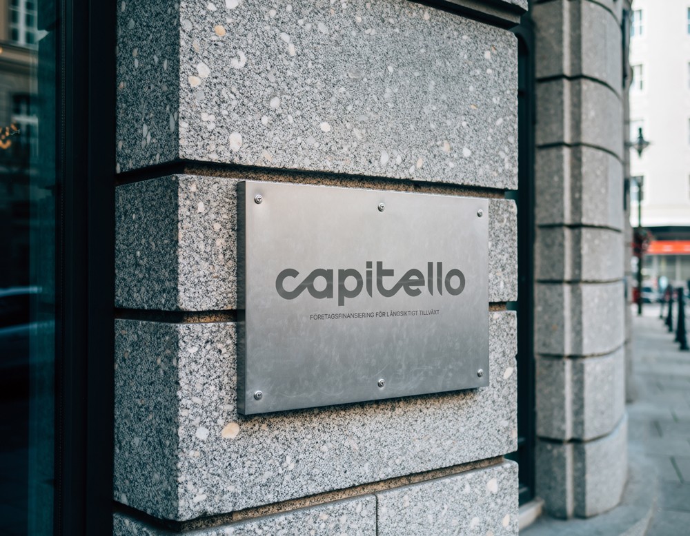 Capitello Finans logo mounted as dimensional lettering on a grey textured exterior wall, demonstrating the brand identity applied to architectural signage.