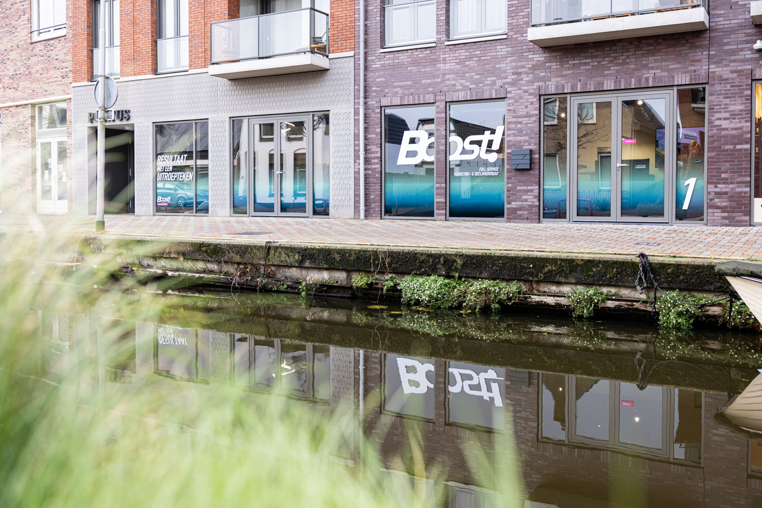 Modern red brick apartment or office building viewed from below against a blue sky, showcasing its geometric architecture with evenly spaced windows and balconies.