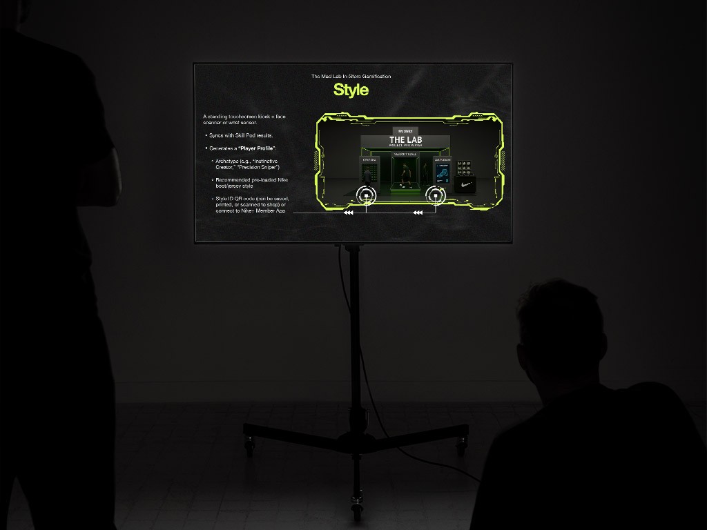 Presentation display showing a Nike pitch concept for interactive in-store gamification, featuring futuristic interface design, neon-accented visuals, and immersive sports-inspired presentation graphics viewed in a darkened room.