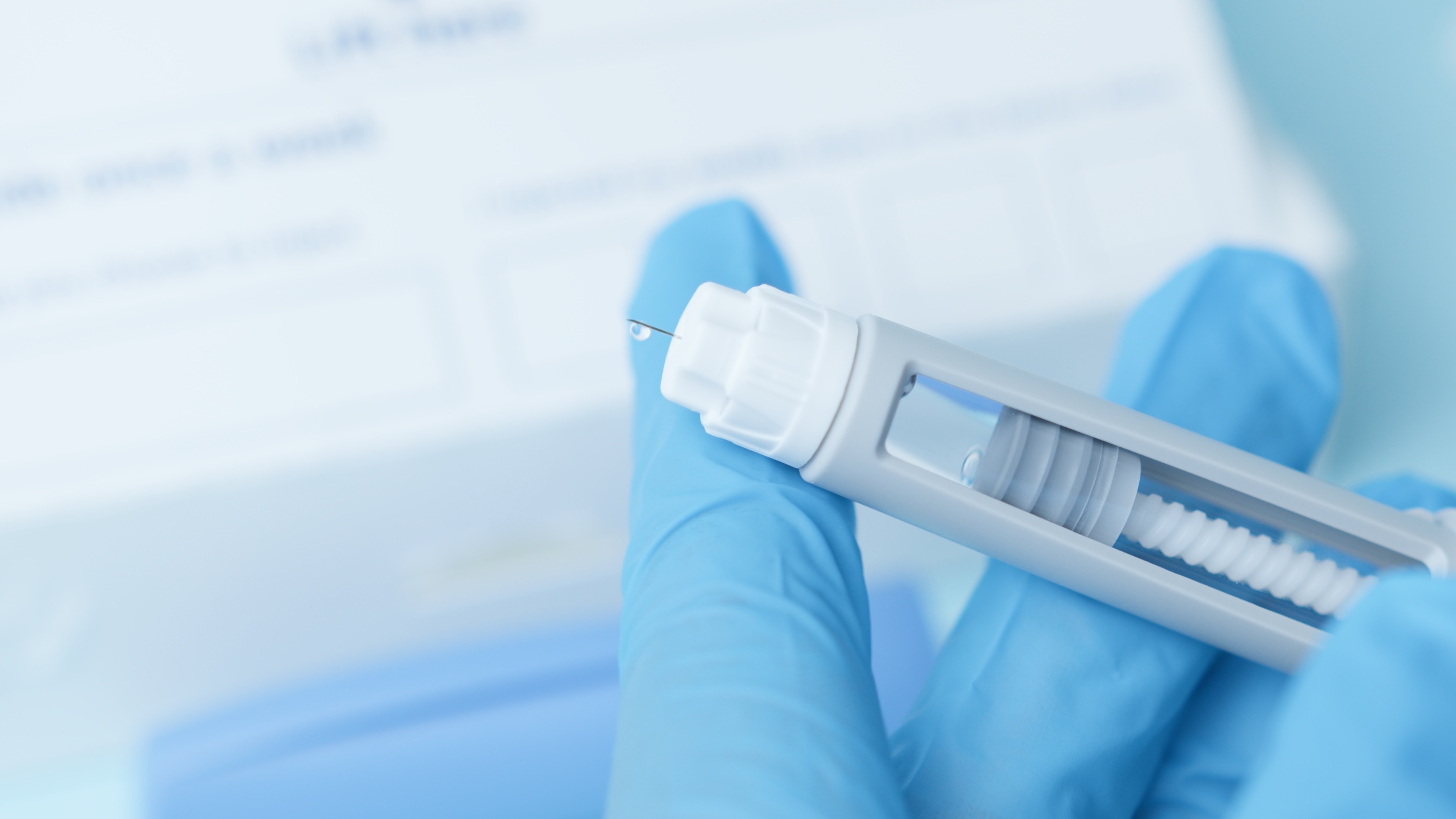 Close up on a needle on diabetic medication pen. Hands with blue glowes taping pen.
