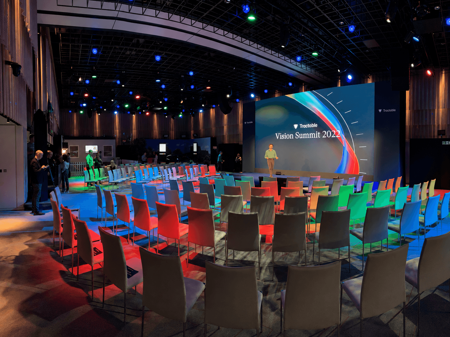 Wide view of the Tractable Vision Summit 2022 conference room with a large LED screen, colourful event lighting and theatre-style seating.