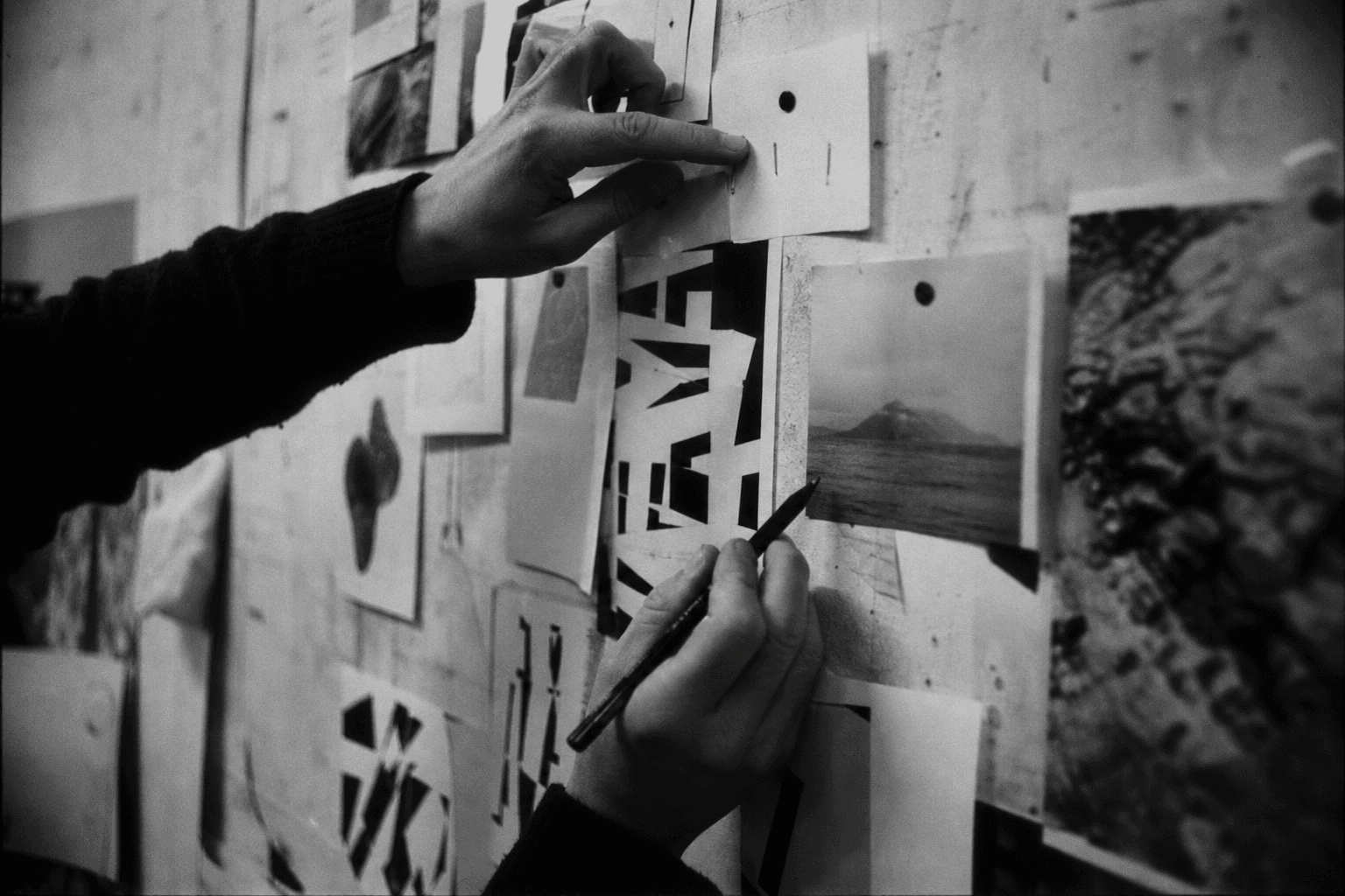 Hands arranging brand strategy and design references on a studio wall in a grainy black and white photograph.