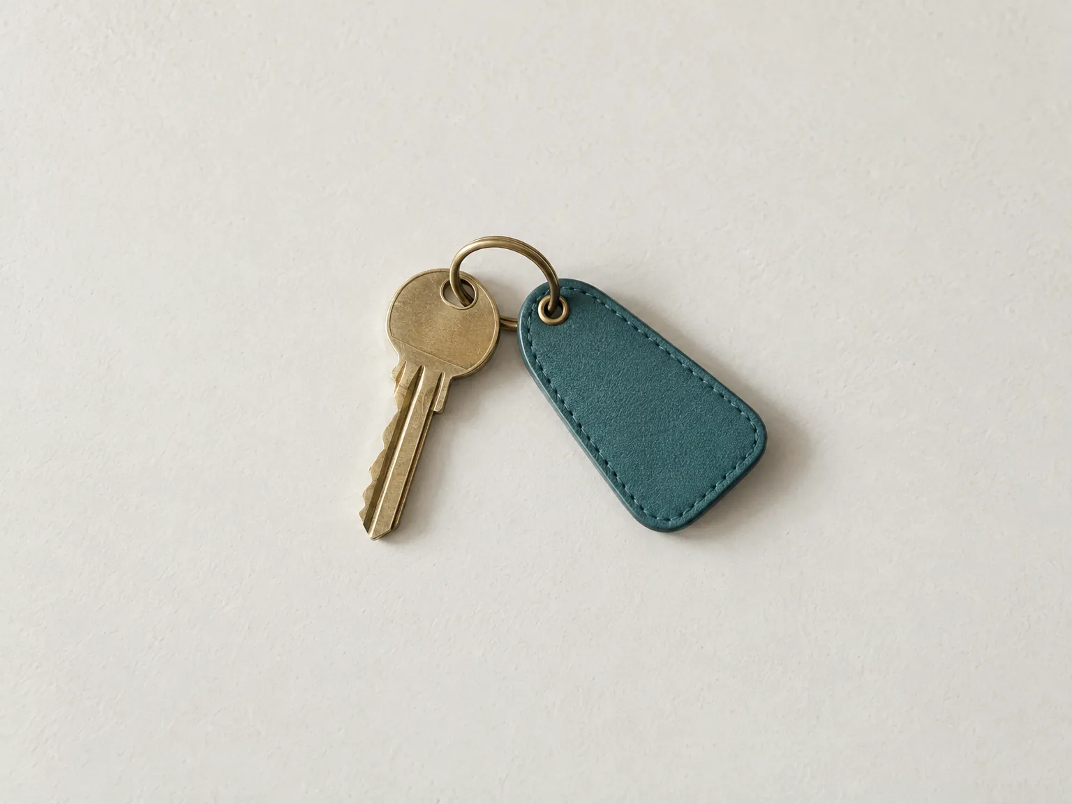 A brass house key with a blank teal leather tag on white plaster