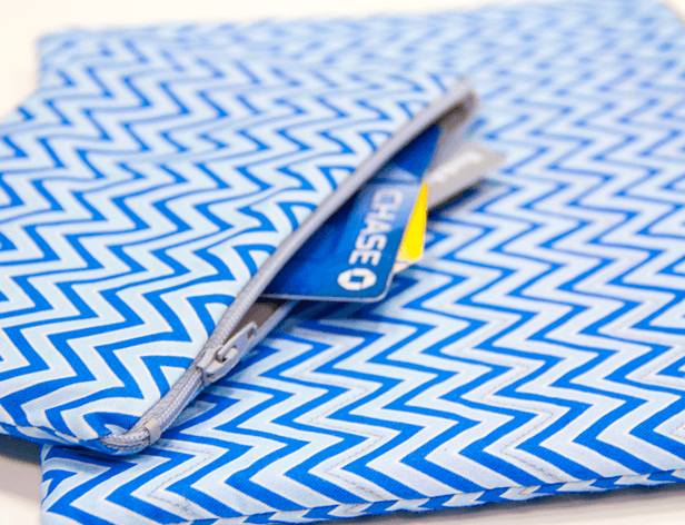 A blue and white chevron-patterned fabric is folded over, revealing a partially zipped blue card inside. The card displays the word “CHASE” in white text and a yellow rectangle beneath it. The folded fabric is positioned diagonally on a white surface.