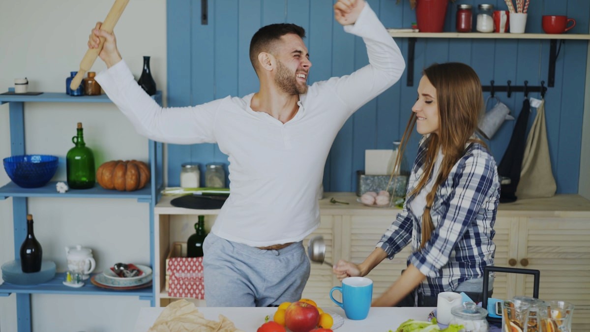 Two people smiling and enjoying cooking together in a home kitchen with fresh produce on the counter