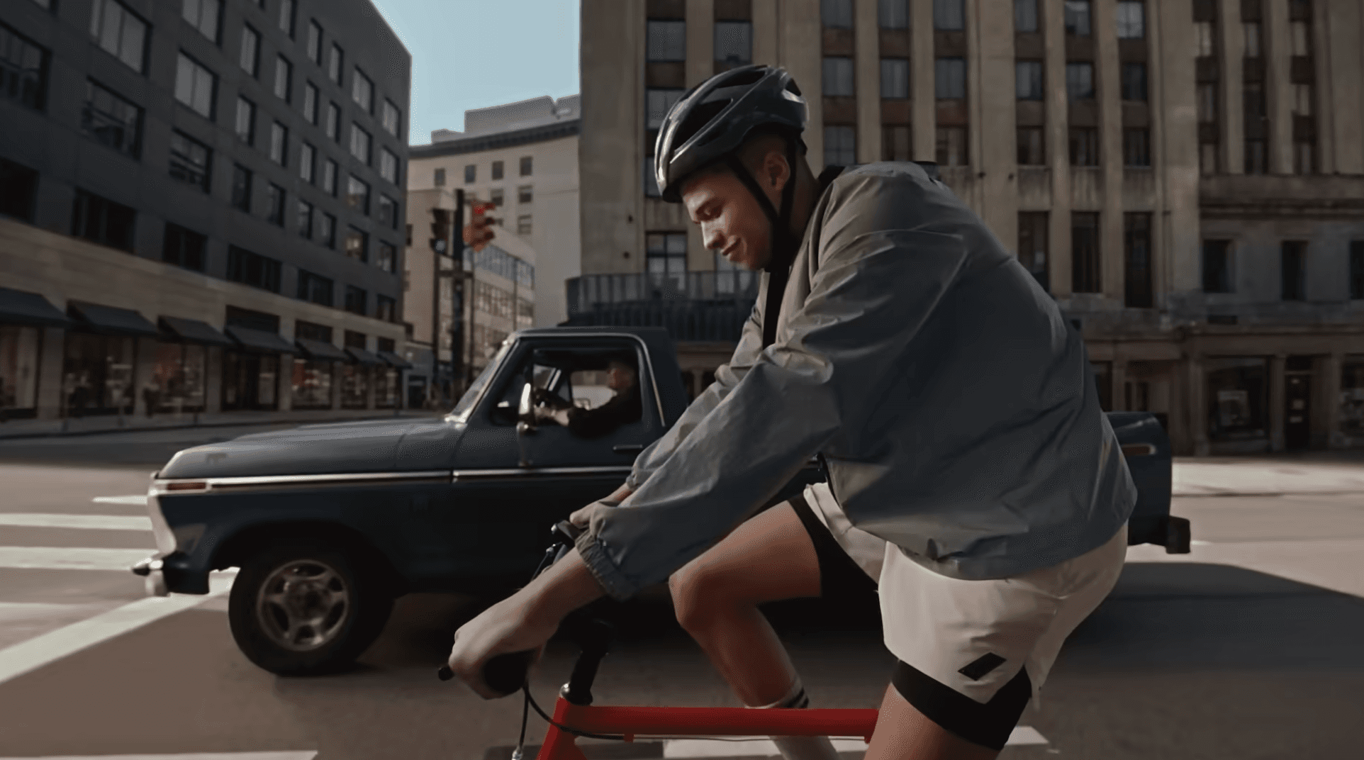 a guy in bicycle standing in the road beside a car in a signal