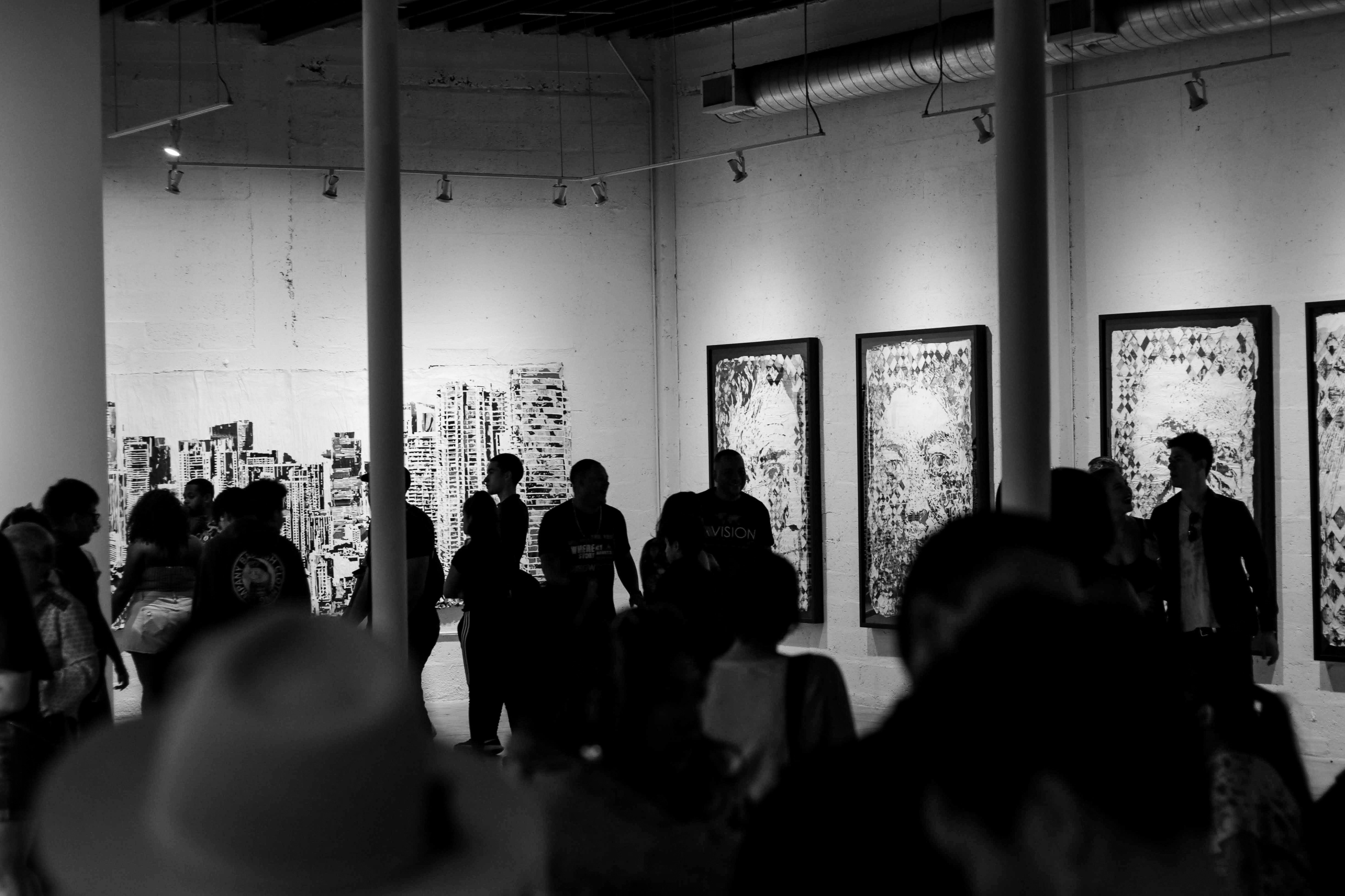 A crowded black-and-white art exhibition with abstract paintings on the walls