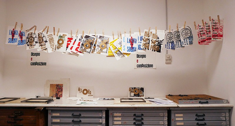 Colorful posters hanged with laundry clips on a wire, above a working bench.