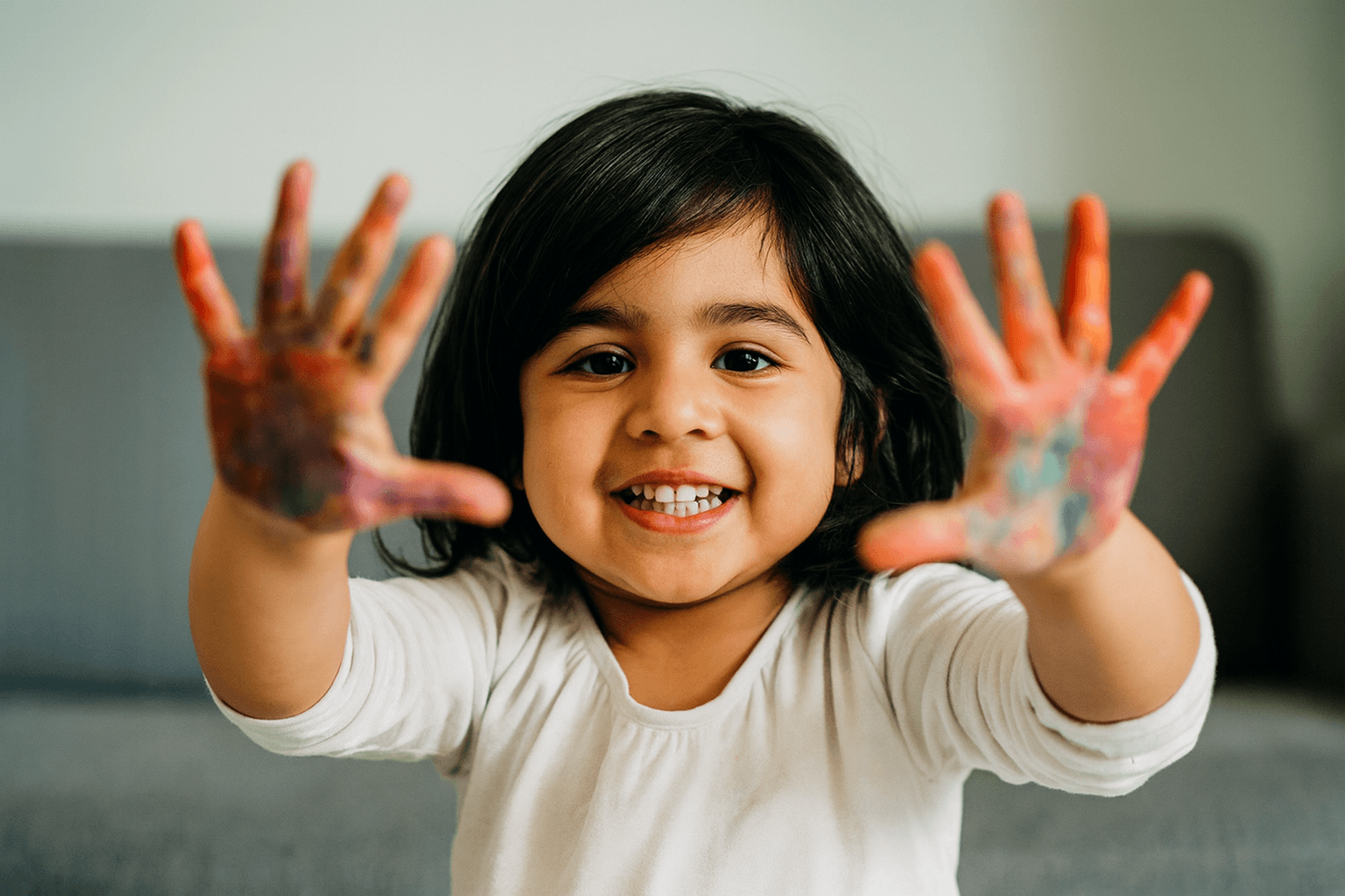 Young girl with painted hands smiling and holding her colorful hands toward the camera during an art activity.