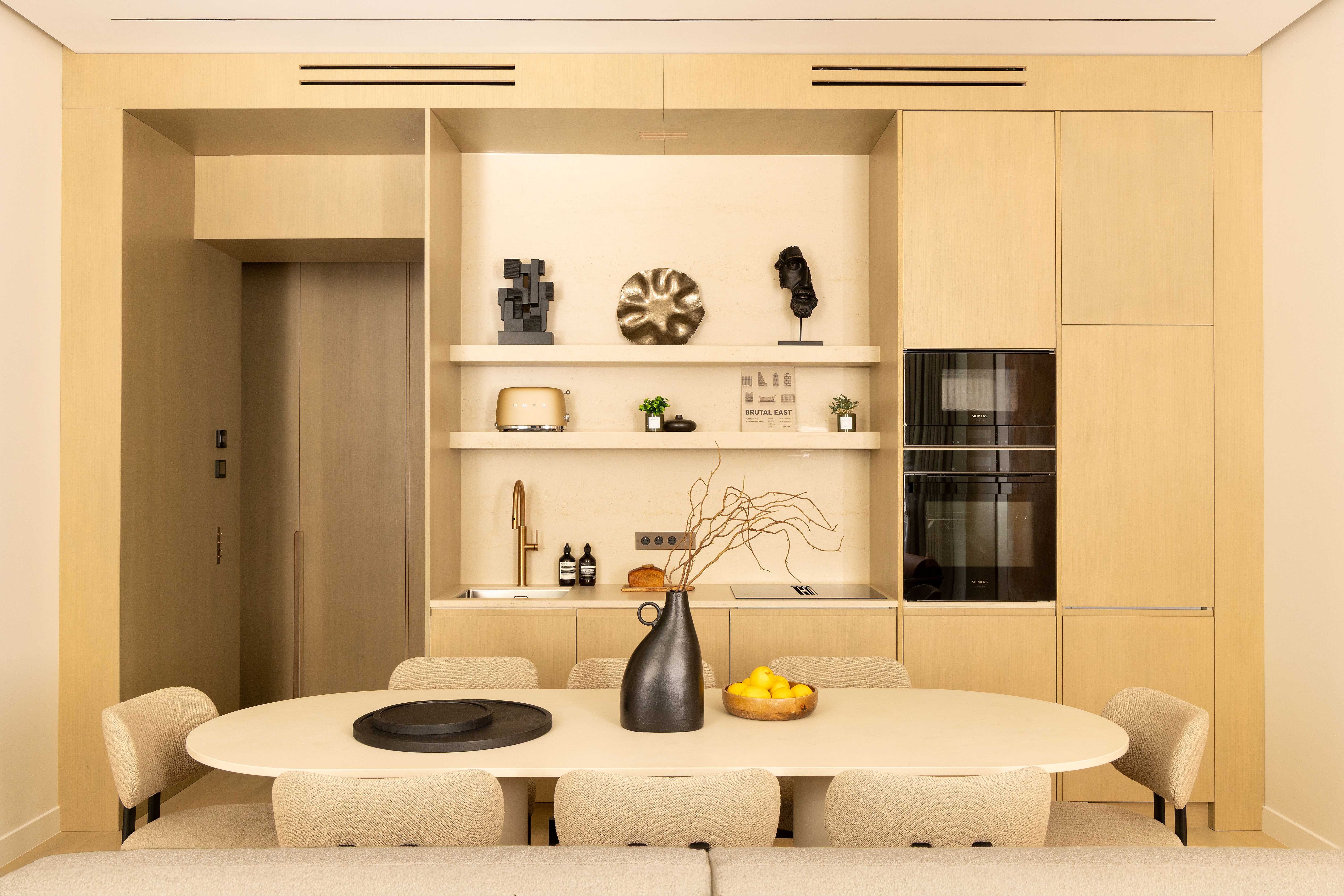 Cuisine intégrée en bois clair vue de face avec table ovale, chaises et objets décoratifs noirs