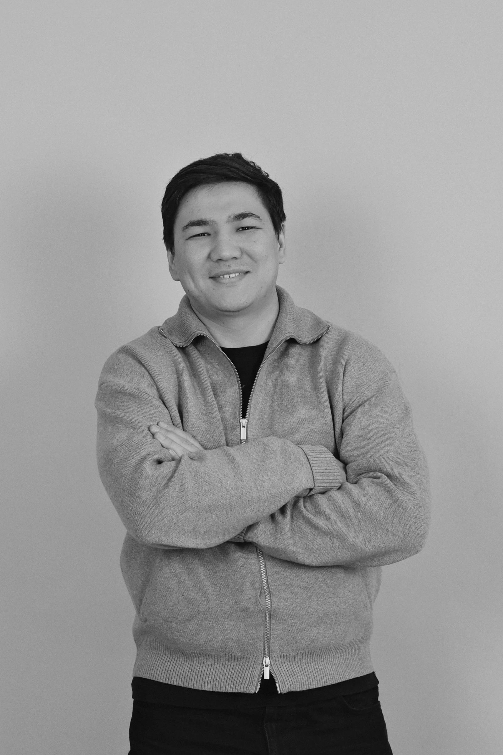 A woman sitting at a desk in a modern office, working on a laptop with documents and plants around her. Sunlight filters through large windows in the background.
