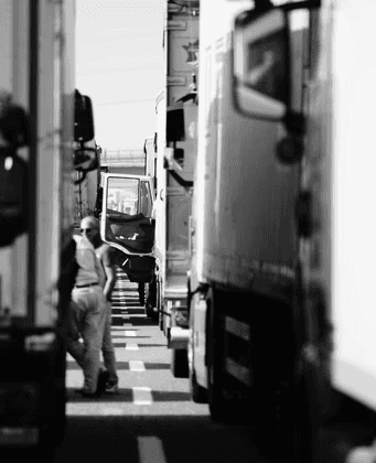 Truck drivers standing between parked semi-trucks on a highway in black and white.