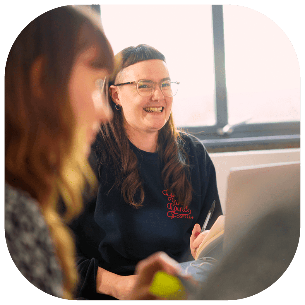 Person seated at a laptop, taking notes during a meeting with another person in the foreground.