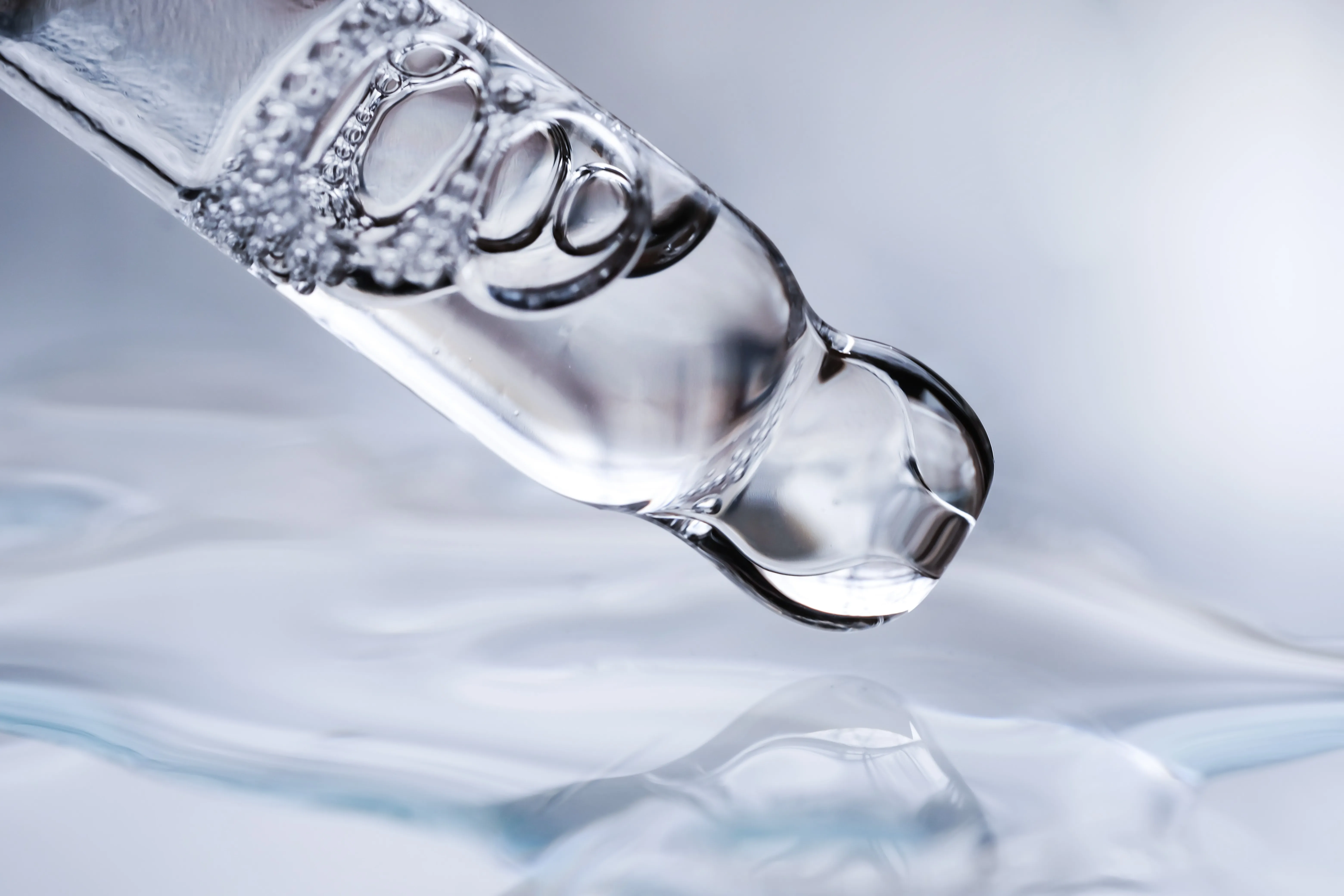 Dropper with liquid and bubbles over water.