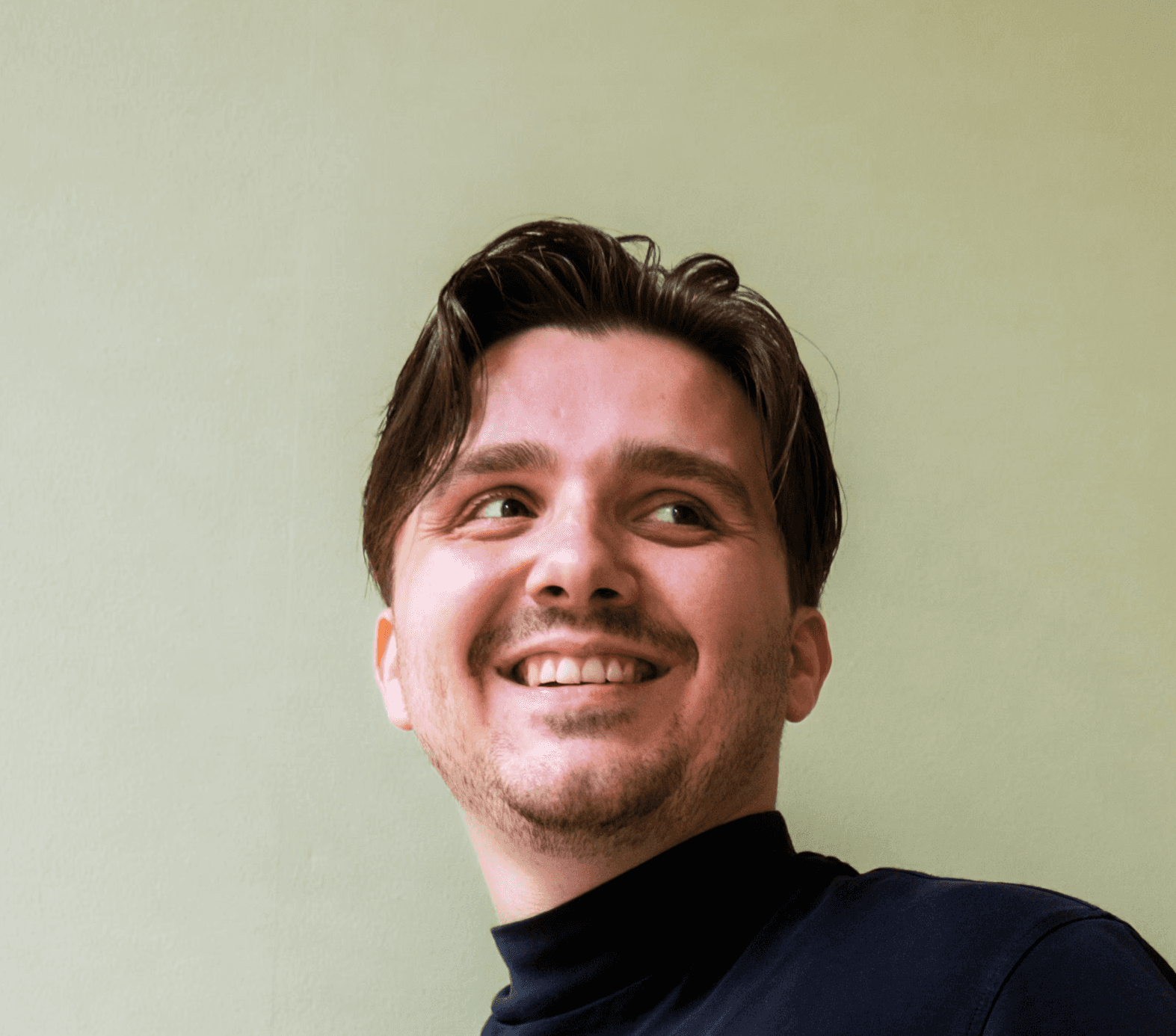 Profilfoto einer lächelnden Person in schwarzer Kleidung vor einem grünen Hintergrund